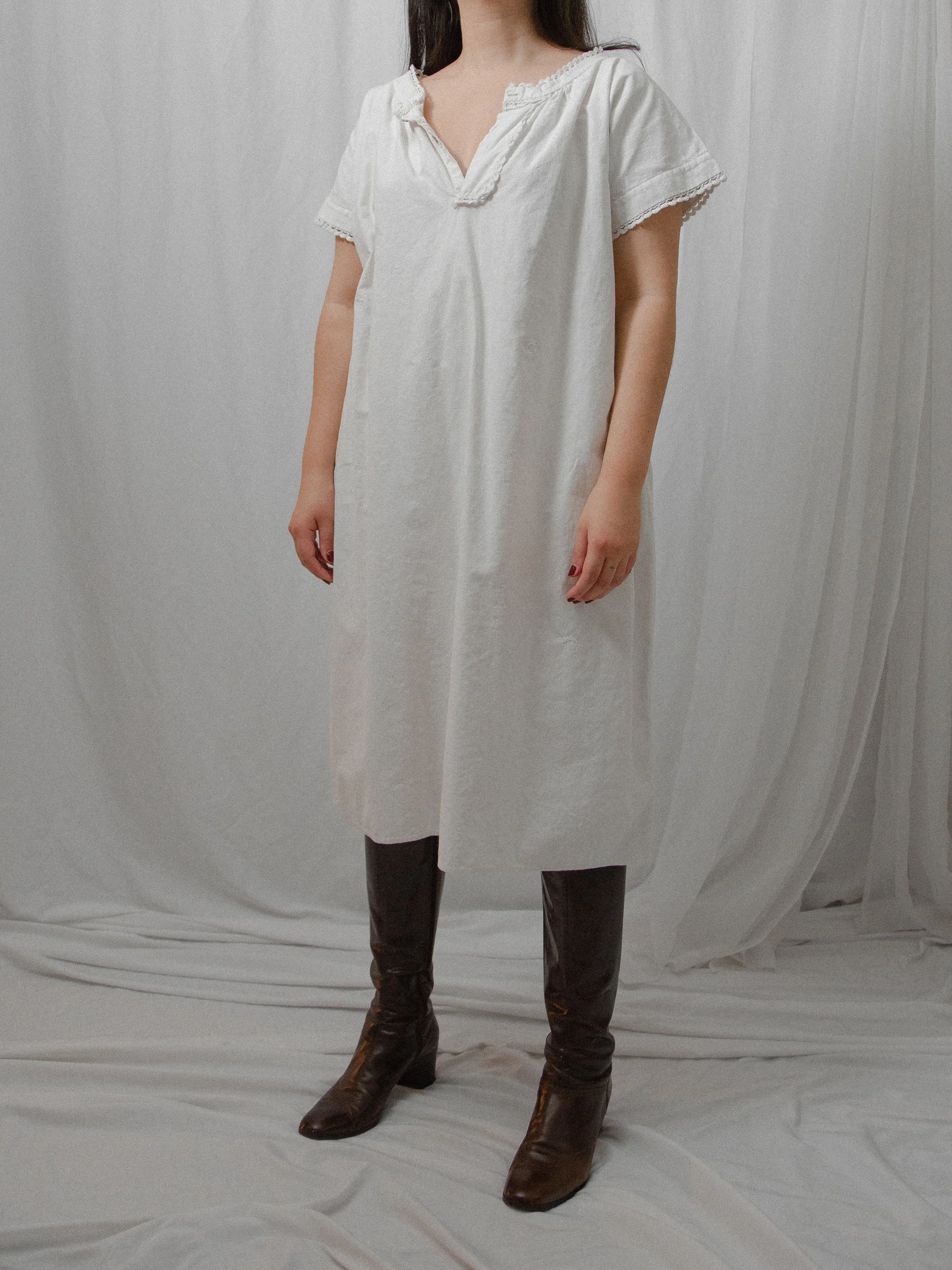 Front view of the 1860s white cotton smock dress worn loose on a model with dark brown boots.