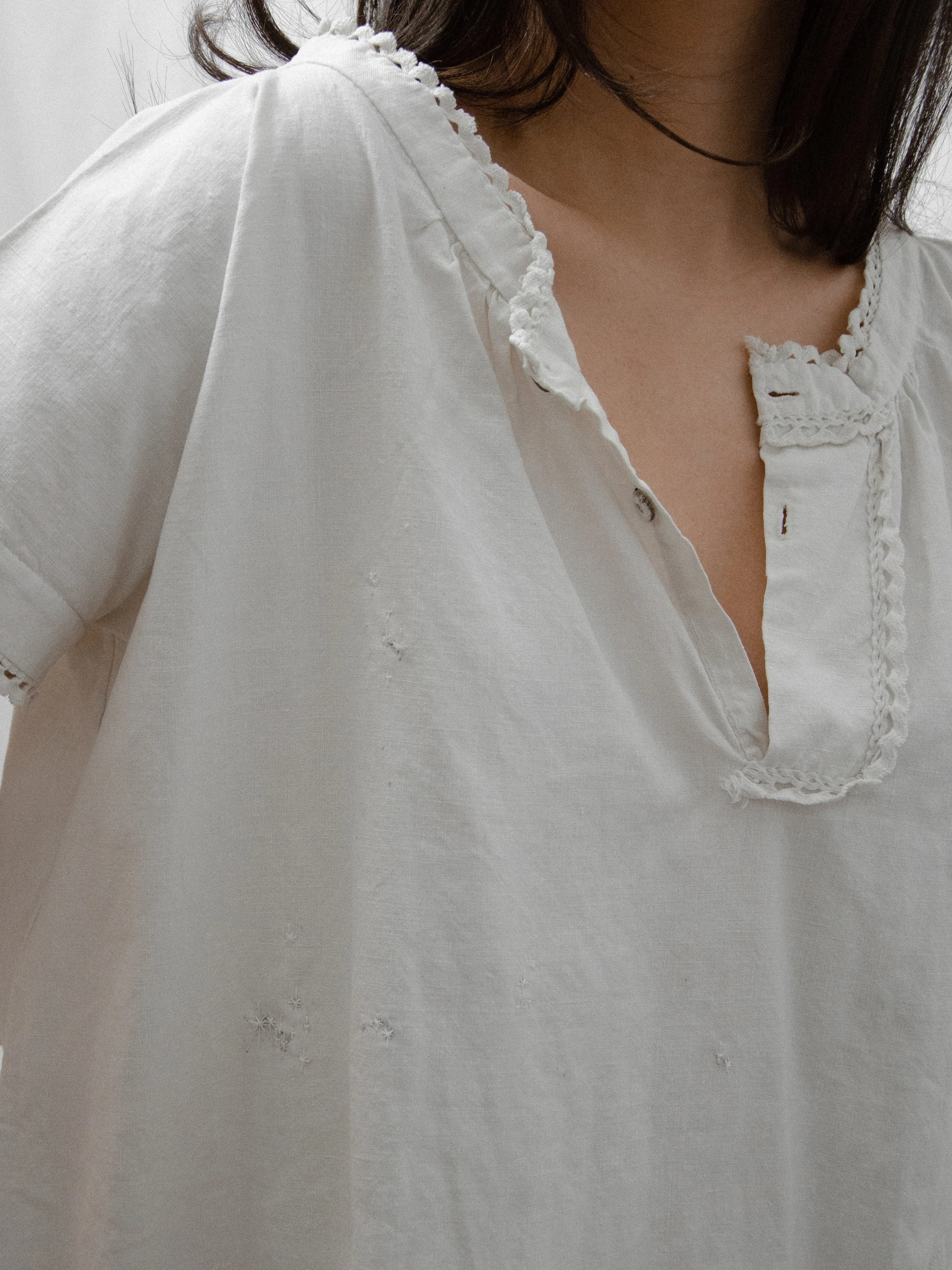 Close-up of the Victorian cotton smock dress's split neckline with lace trim and small metal buttons.