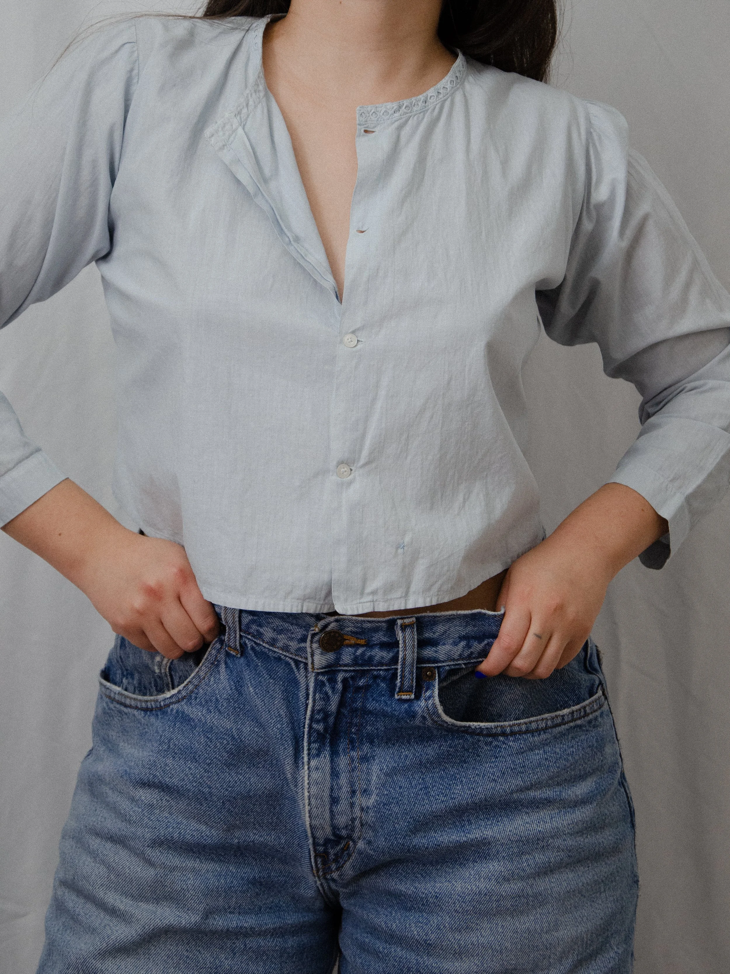 Front view of the light blue antique cotton top worn partly unbuttoned on a model with hands in pockets.