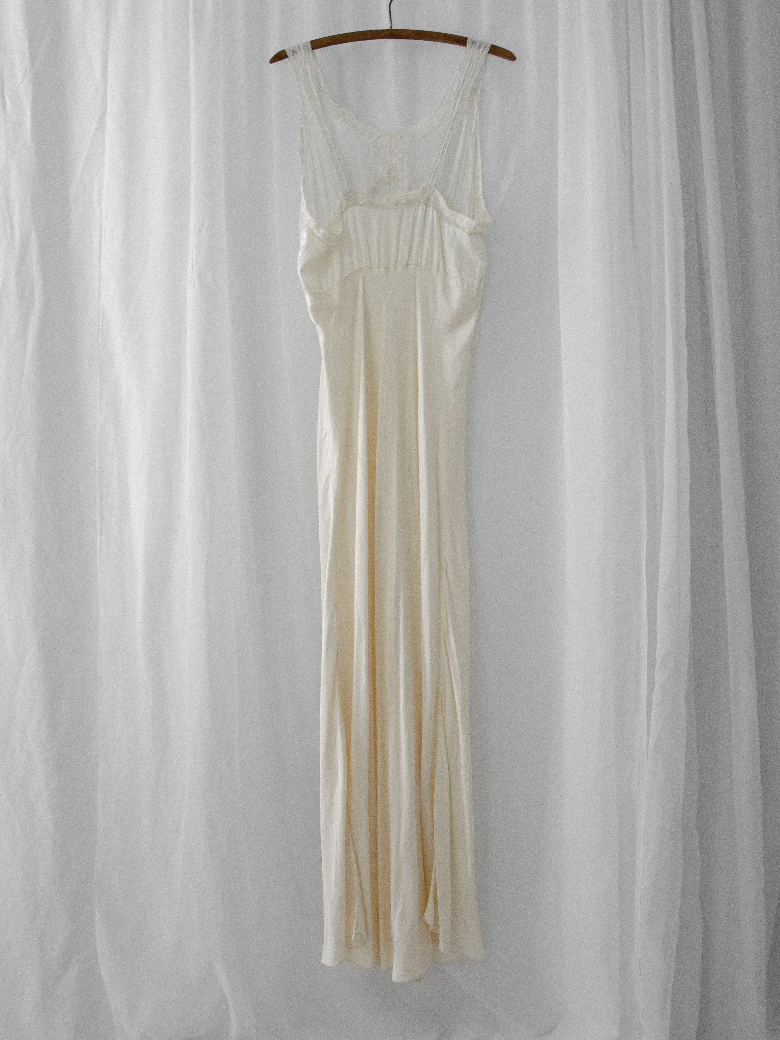 1930s ivory silk bias-cut slip dress on a wooden hanger, full-length view.