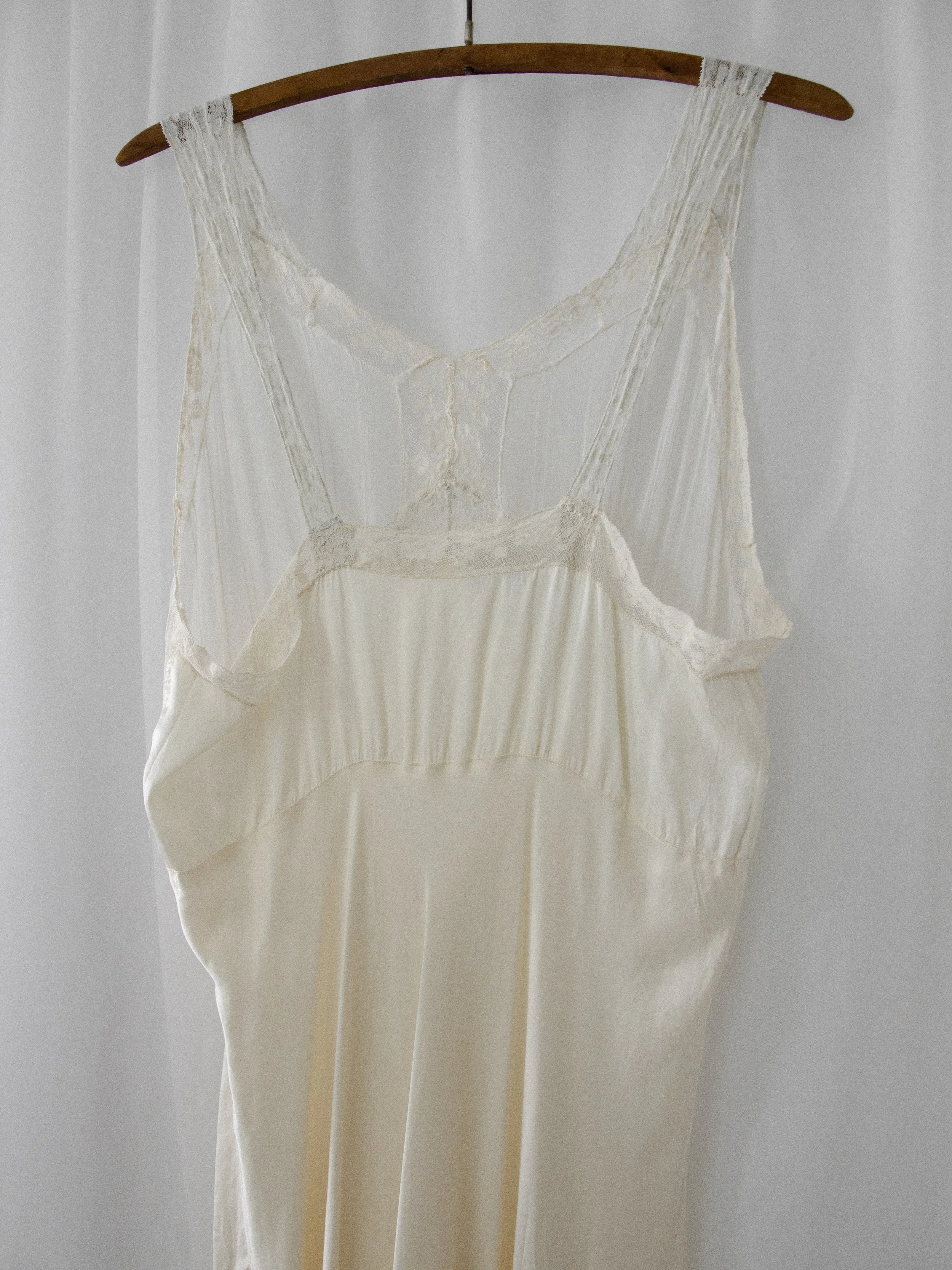 Close-up of the 1930s ivory silk slip dress on a hanger, showing the sheer lace and pintucked upper panel.