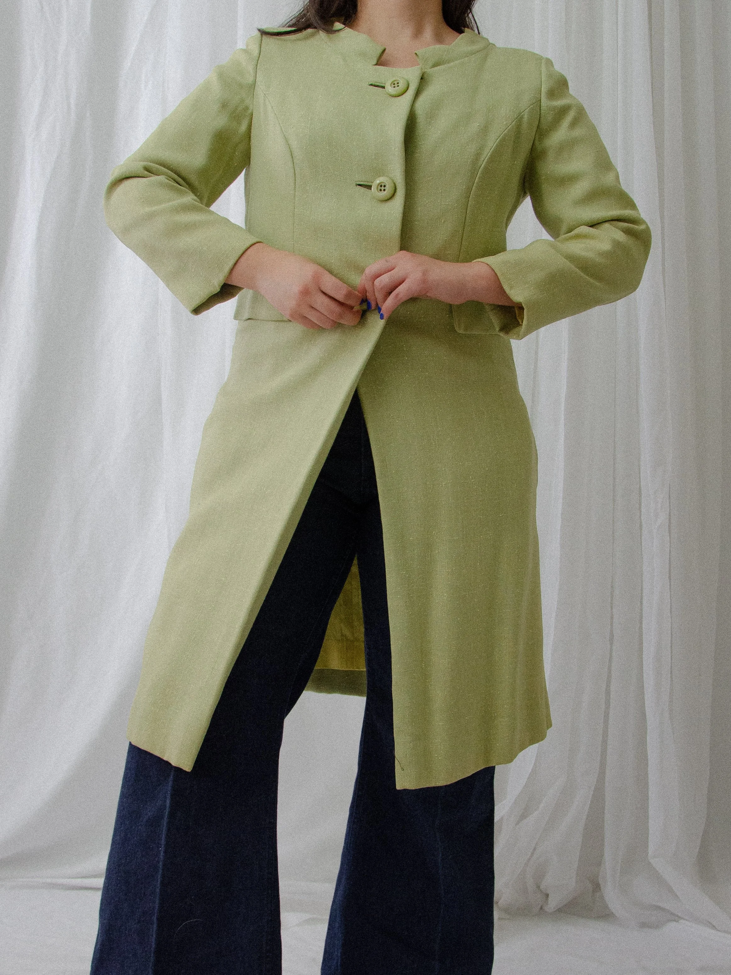 1950s light green linen coat on a model buttoning the front, showing the collarless neckline and lining.