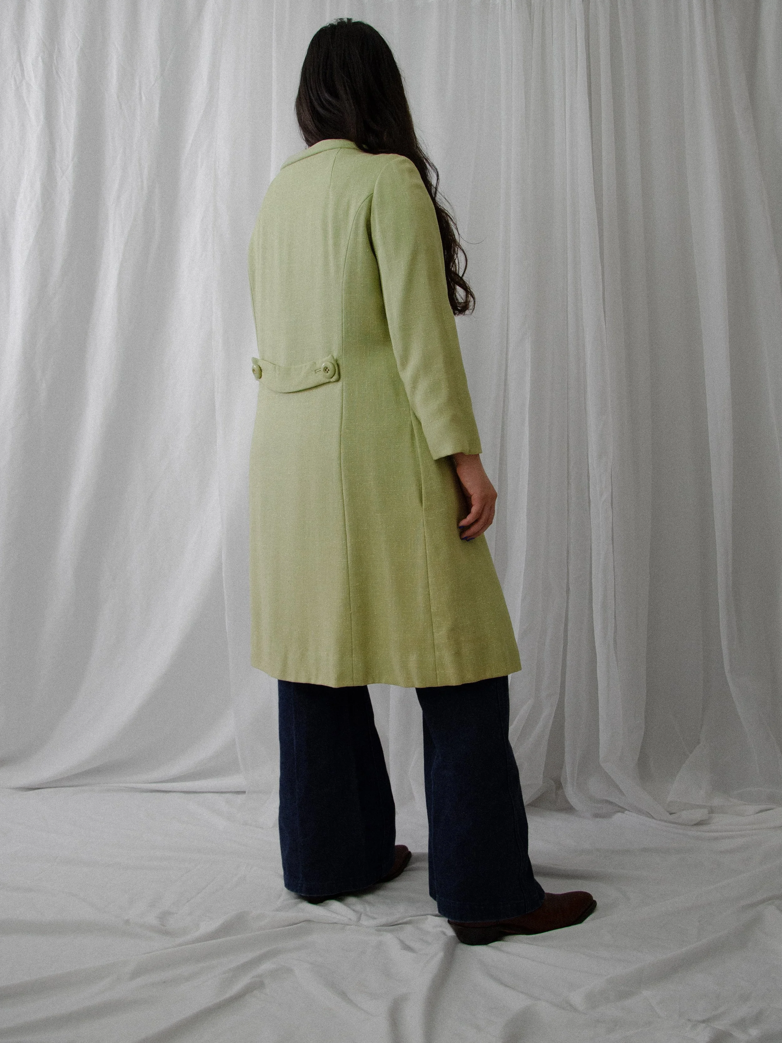 Back view of the 1950s pistachio green linen coat on a model, showing the buttoned back half belt.