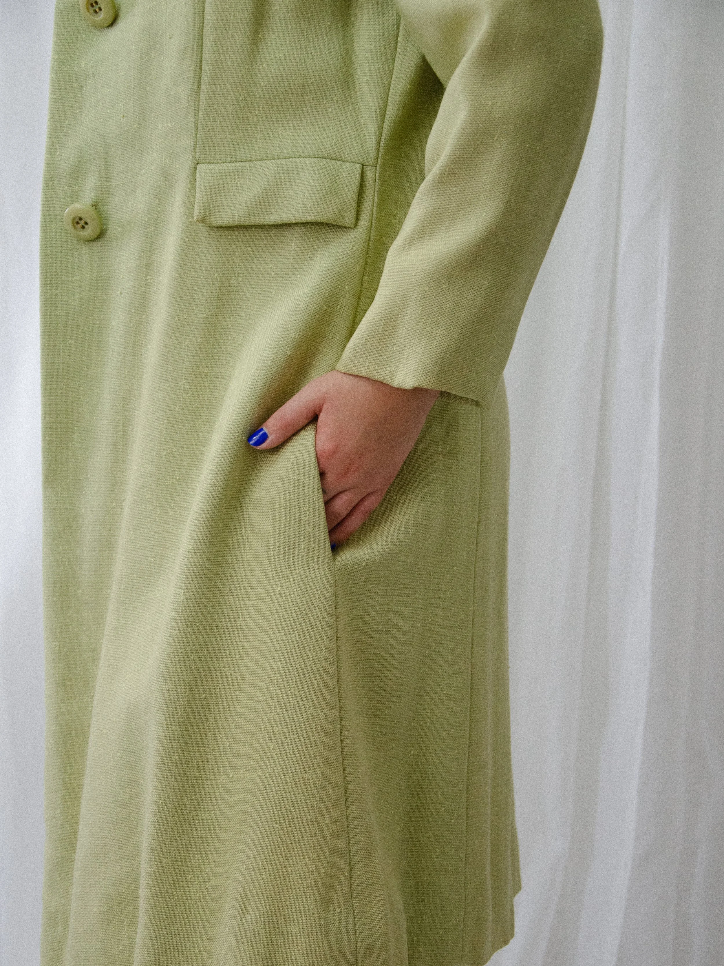 Close-up of the 1950s pistachio linen coat's decorative pocket flap, with a hand in the side pocket below.