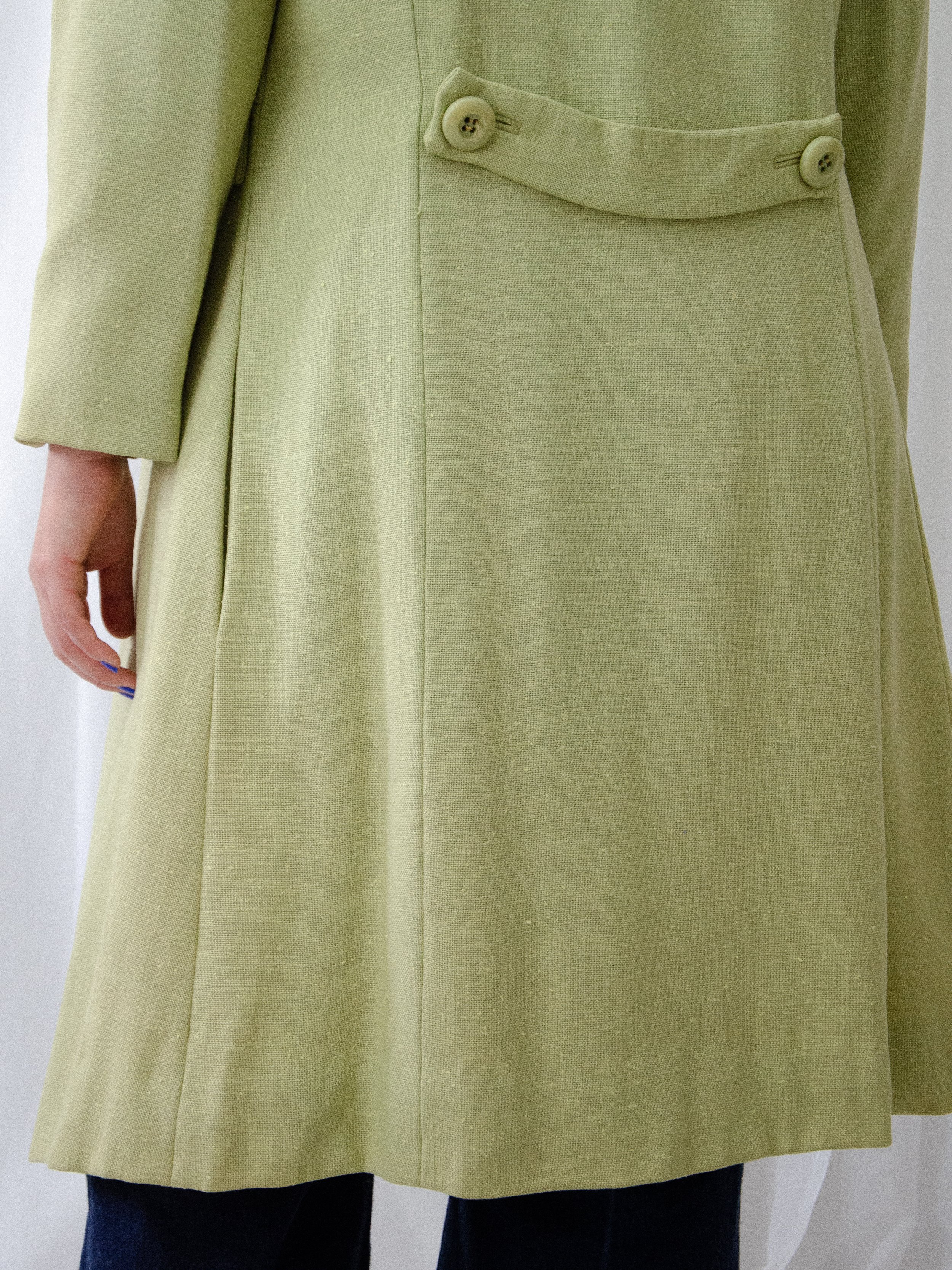 Detail of the 1950s green linen coat's back, showing a buttoned half belt and seamed flared skirt.