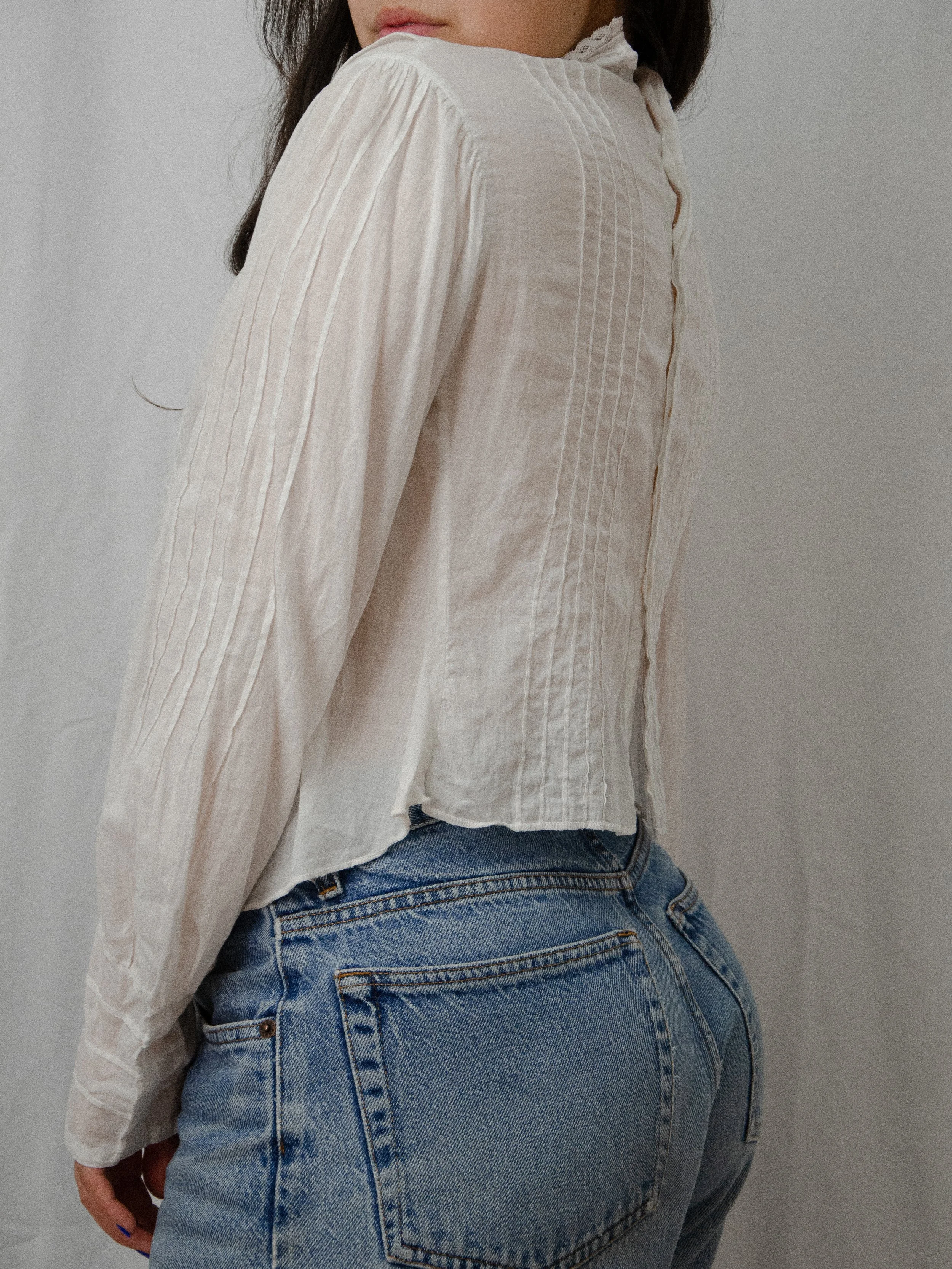 Side-back view of the 1910s white cotton mock neck top on a model, showing the back buttons and pintucks.