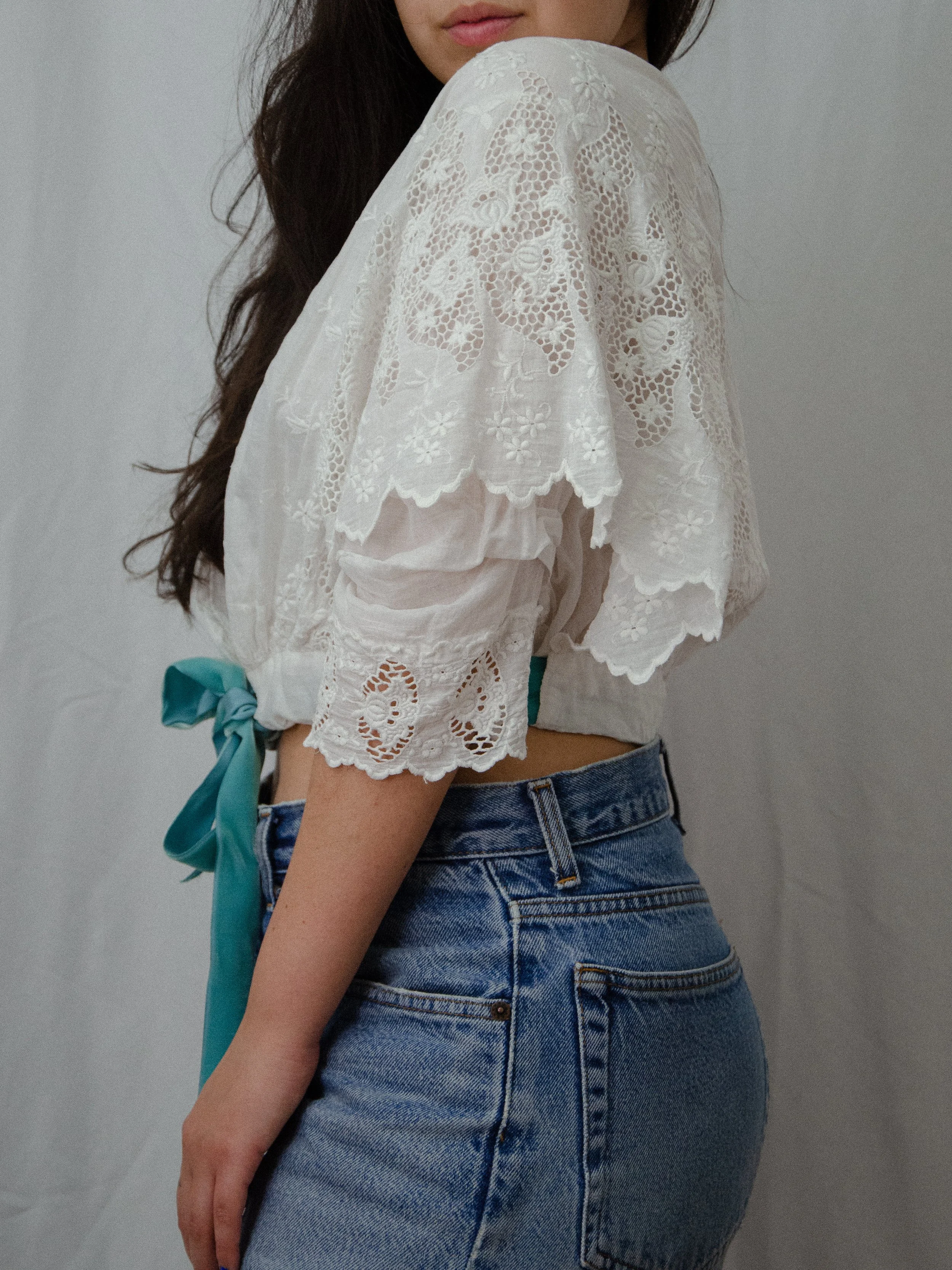 Side view of the antique white wrap blouse on a model, showing the cropped length and aqua ribbon.