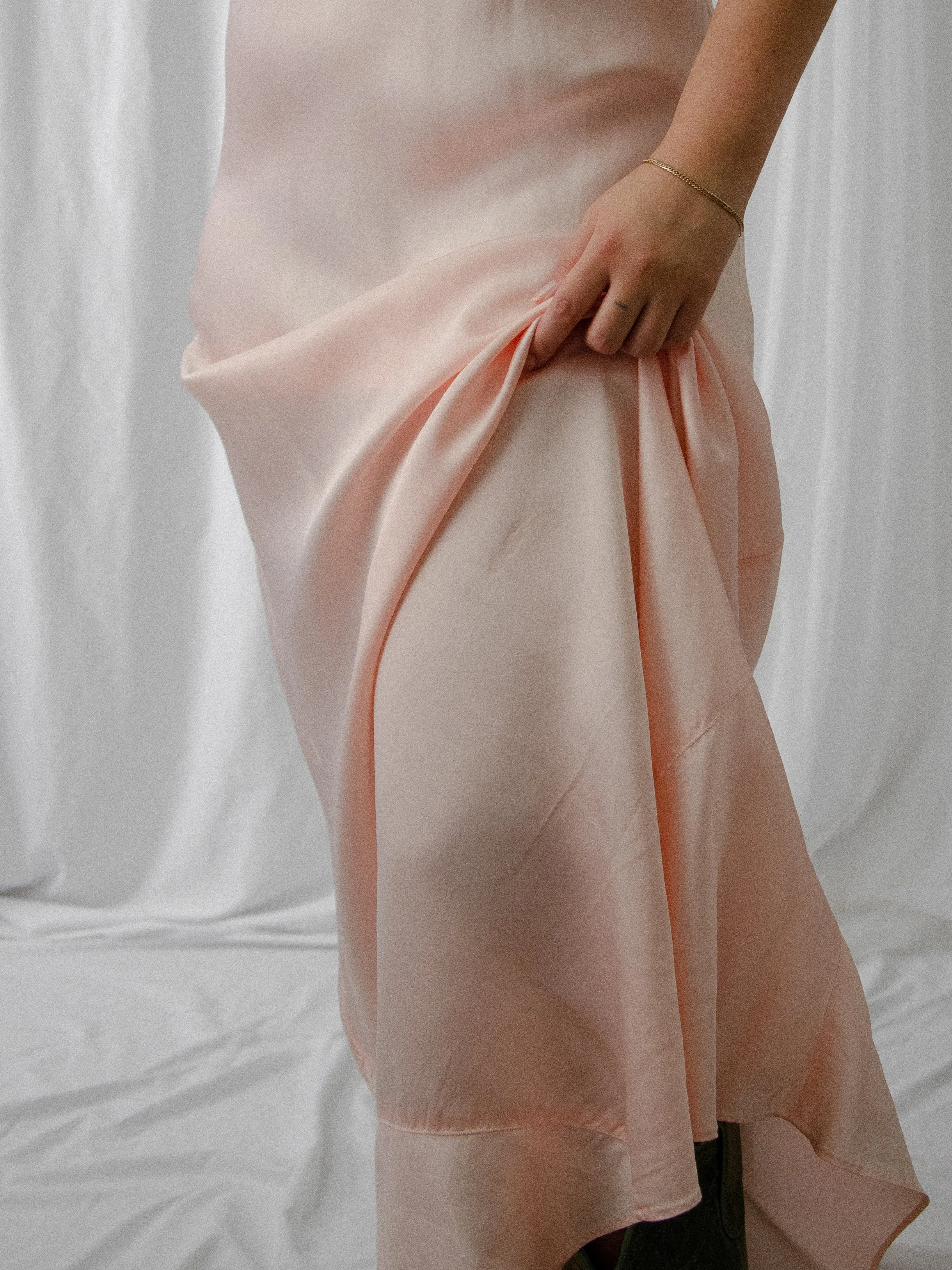 Detail of the 1940s pink satin slip dress skirt gathered in hand, showing the satin sheen.