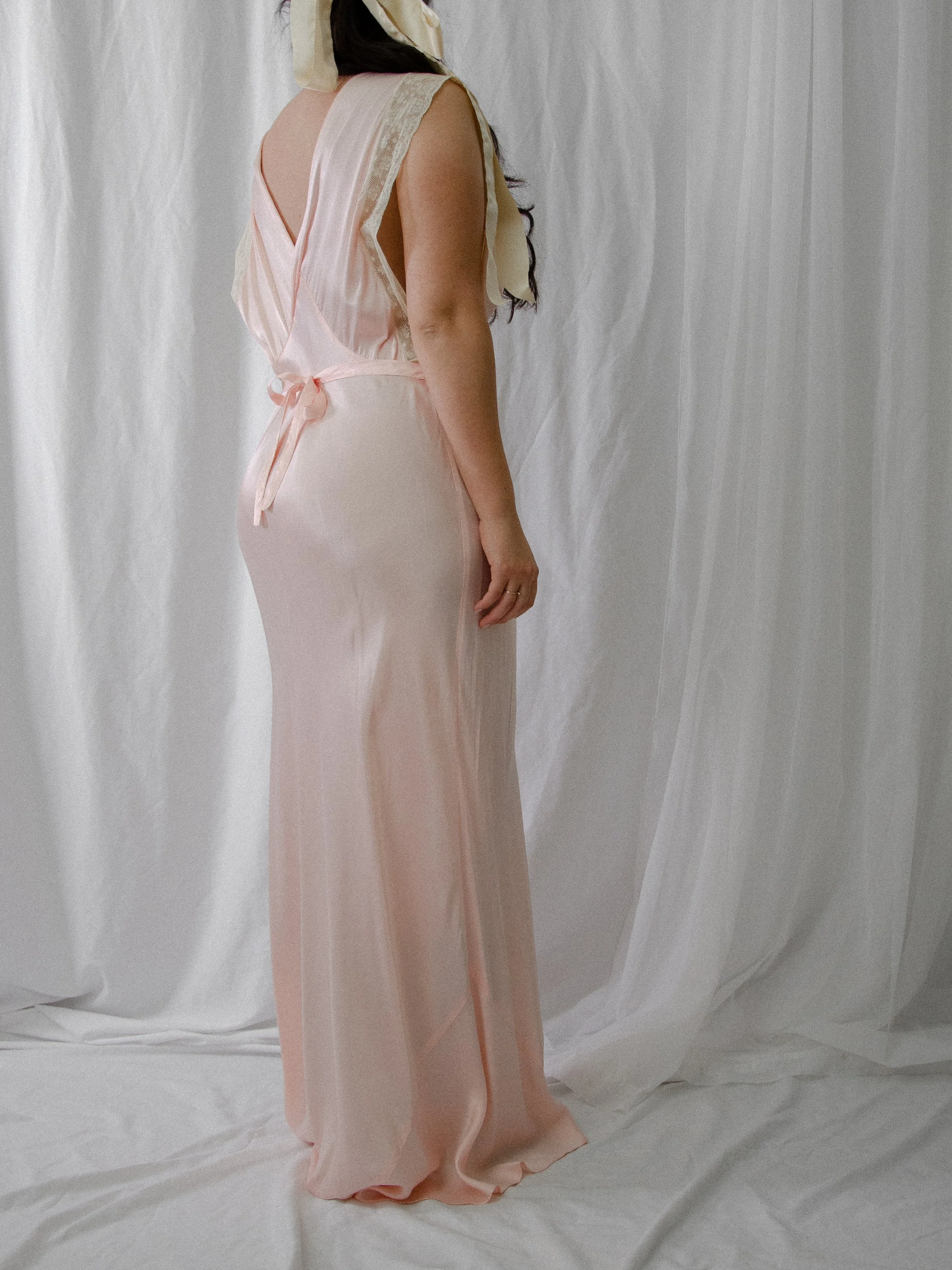 Back view of the 1940s baby pink satin slip dress on a model, showing the open back and tie.