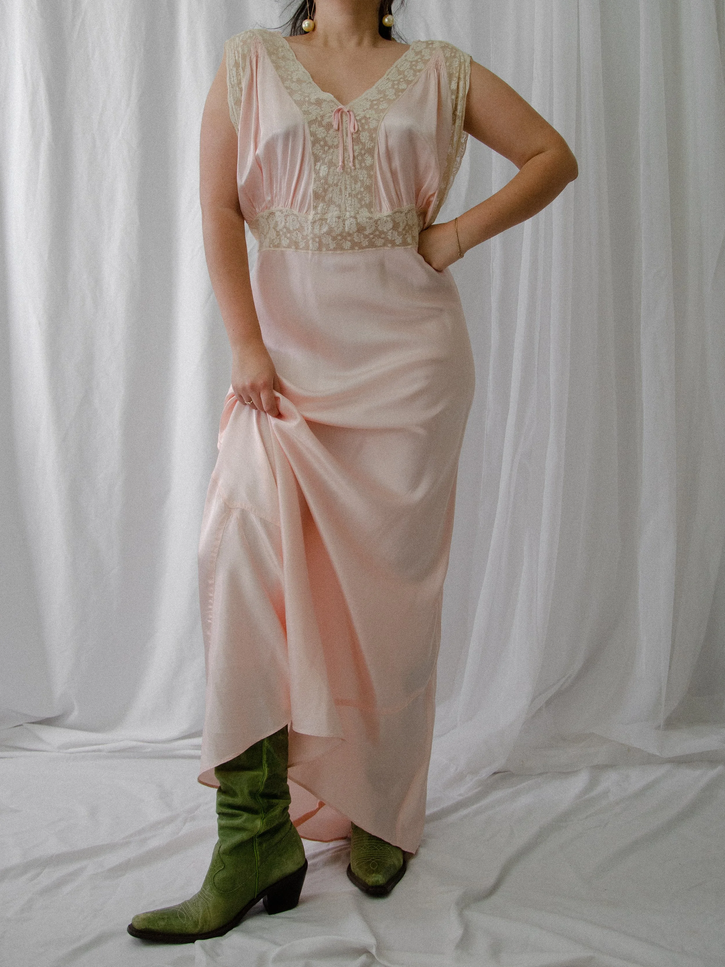 1940s baby pink satin slip dress on a model holding up the skirt to show green boots.