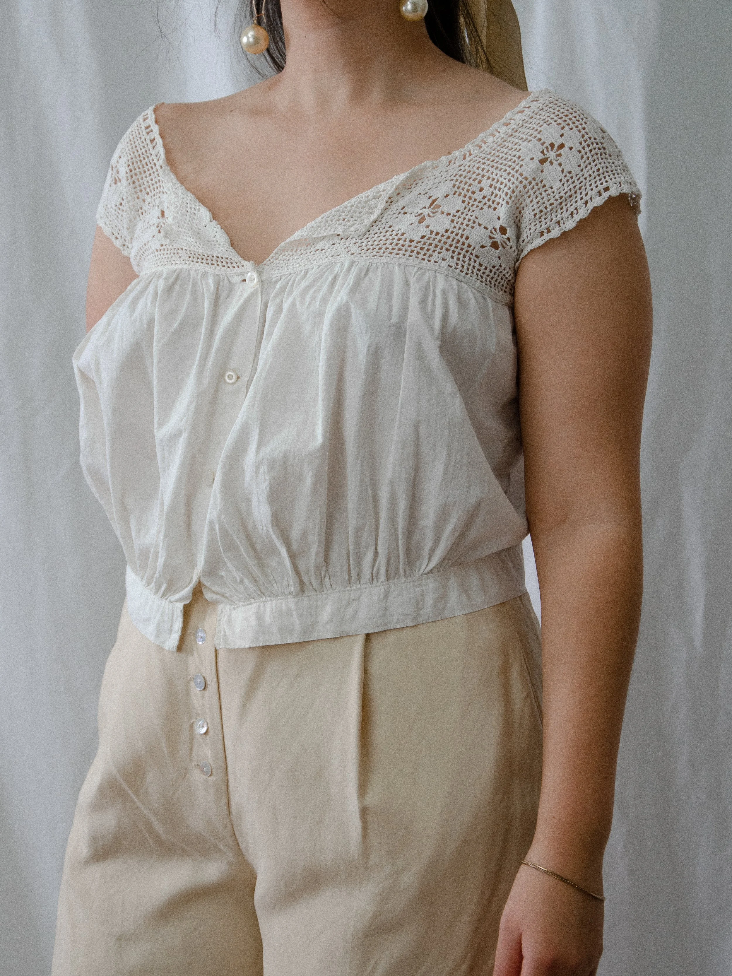Three-quarter view of the antique white cotton crochet tank on a model, showing the cropped banded waist.