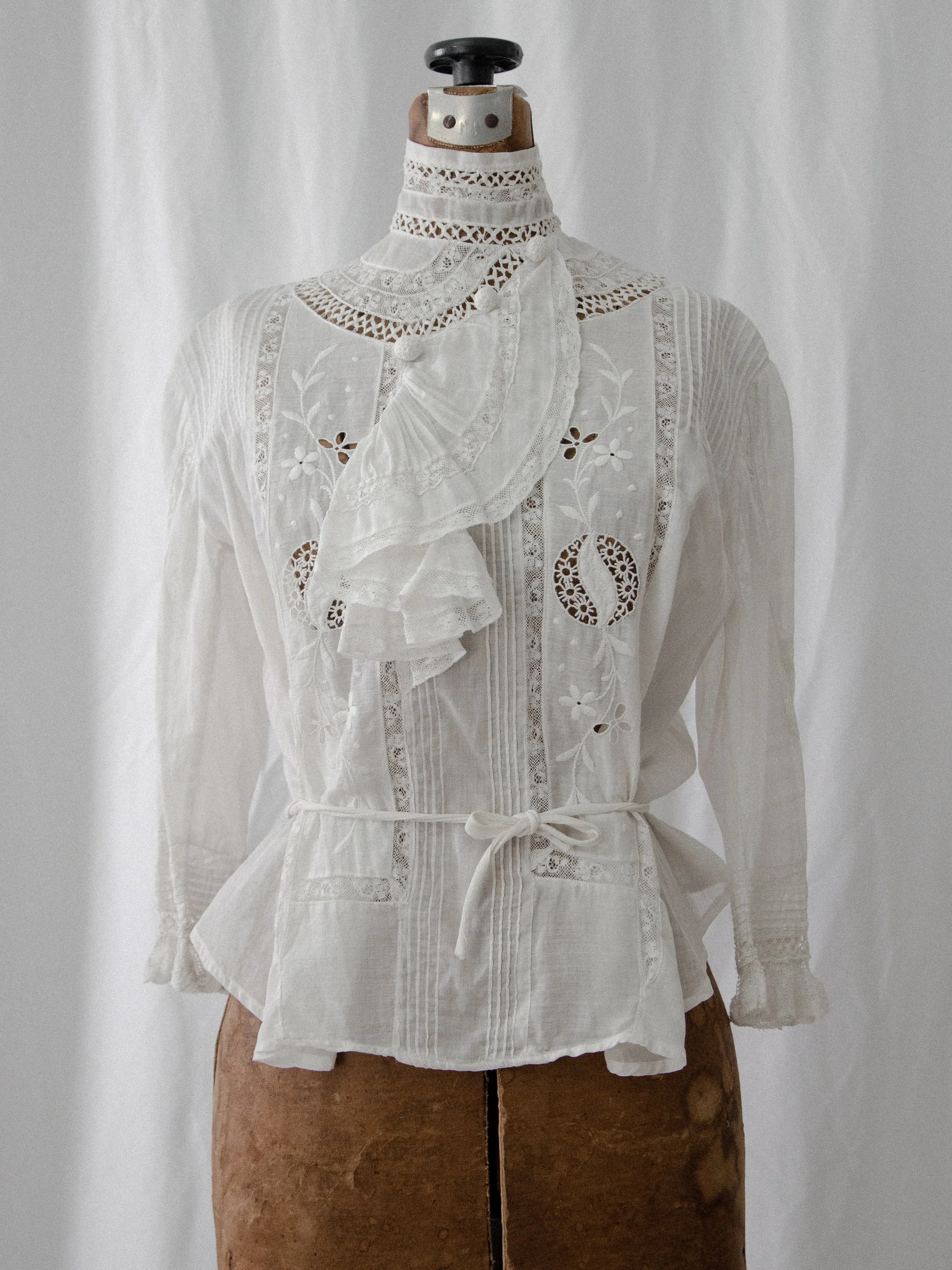 Edwardian white cotton ascot blouse with mock neck and waist tie on a dress form, front view.