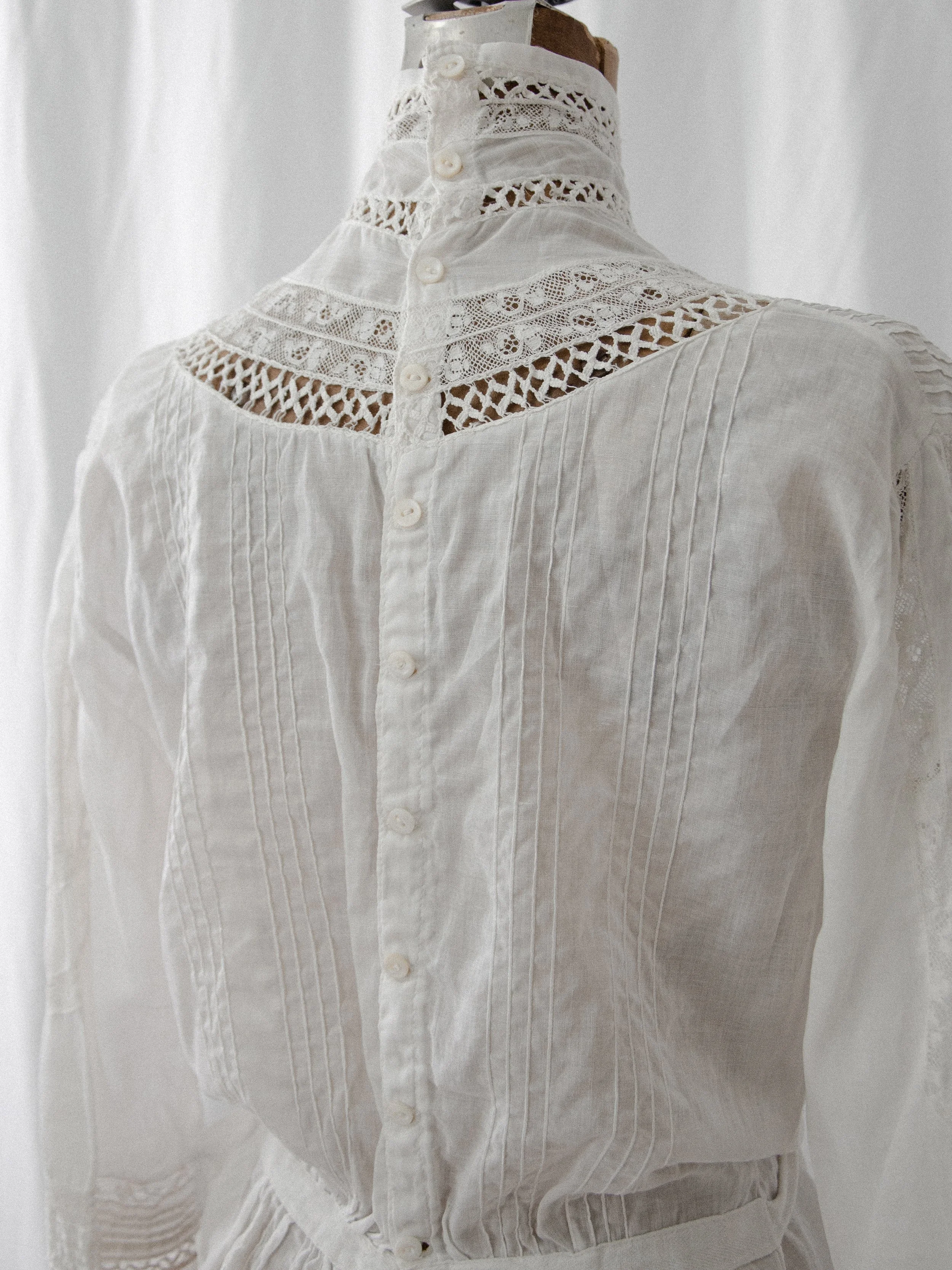 Back view of the 1910s white cotton blouse on a dress form, showing the button back and lace yoke.