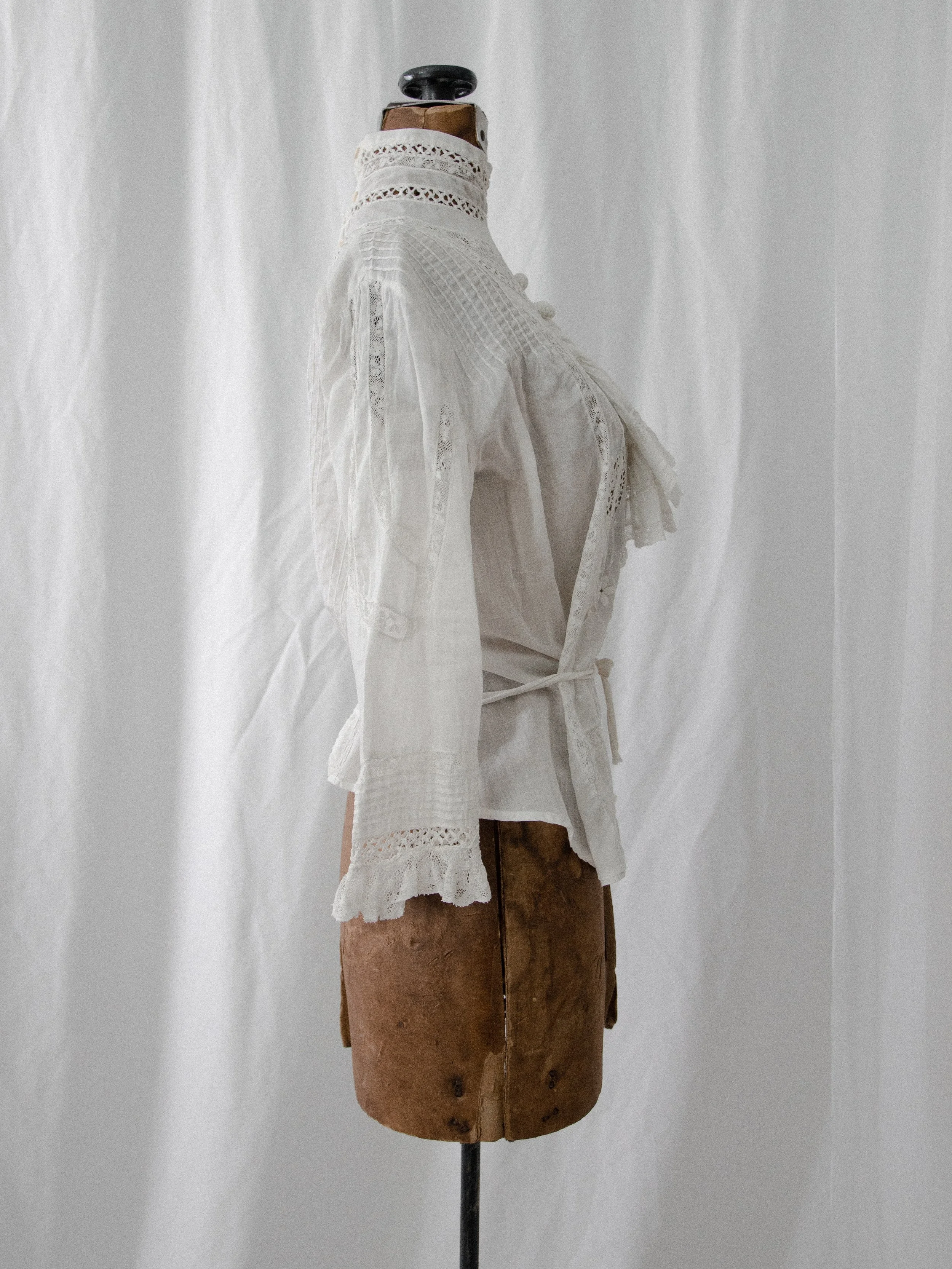 Side view of the 1910s white ascot blouse on a dress form, showing the waist tie and sleeve.