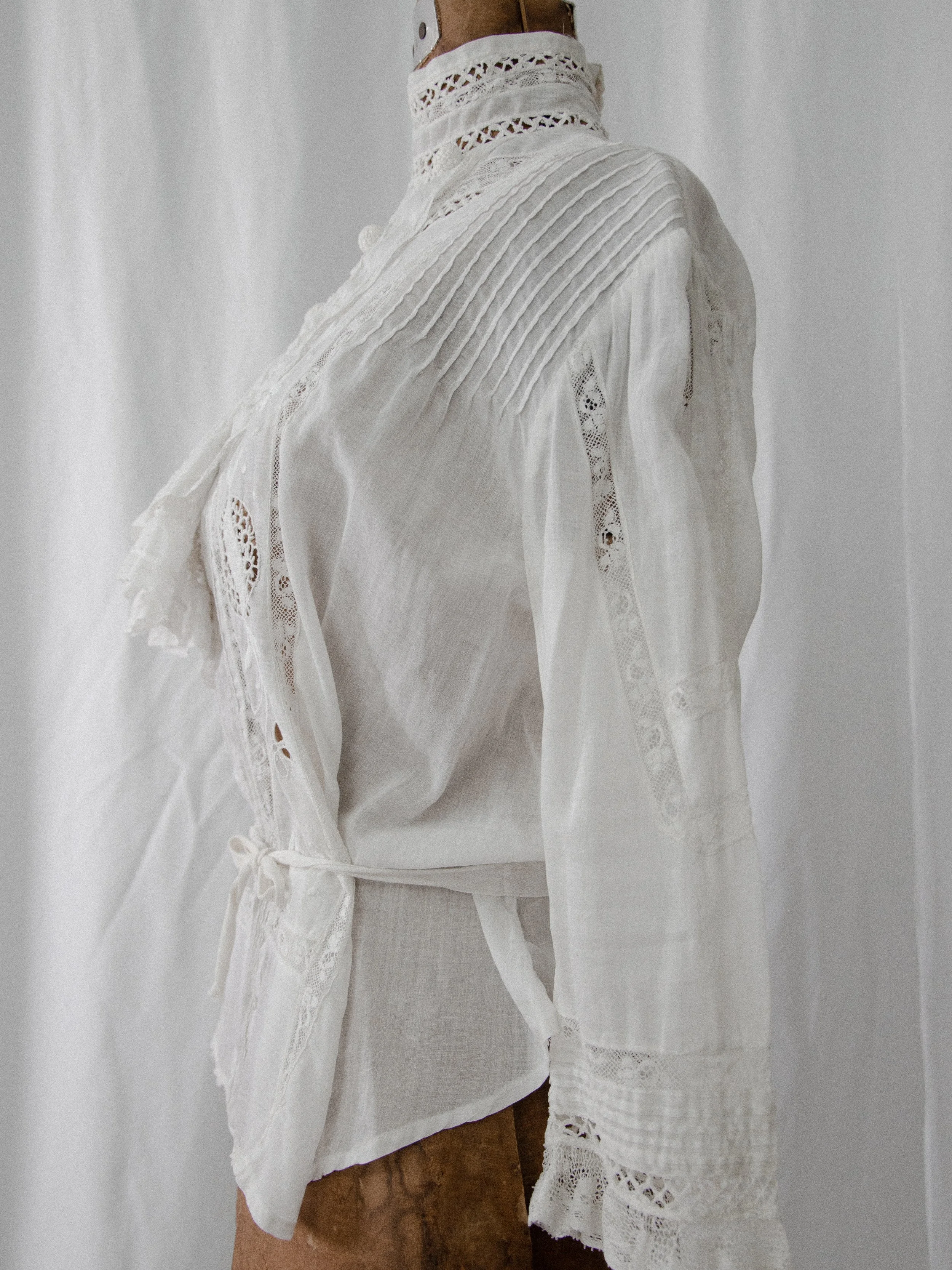 Three-quarter back view of the Edwardian white cotton blouse on a dress form, showing pintucks and lace.