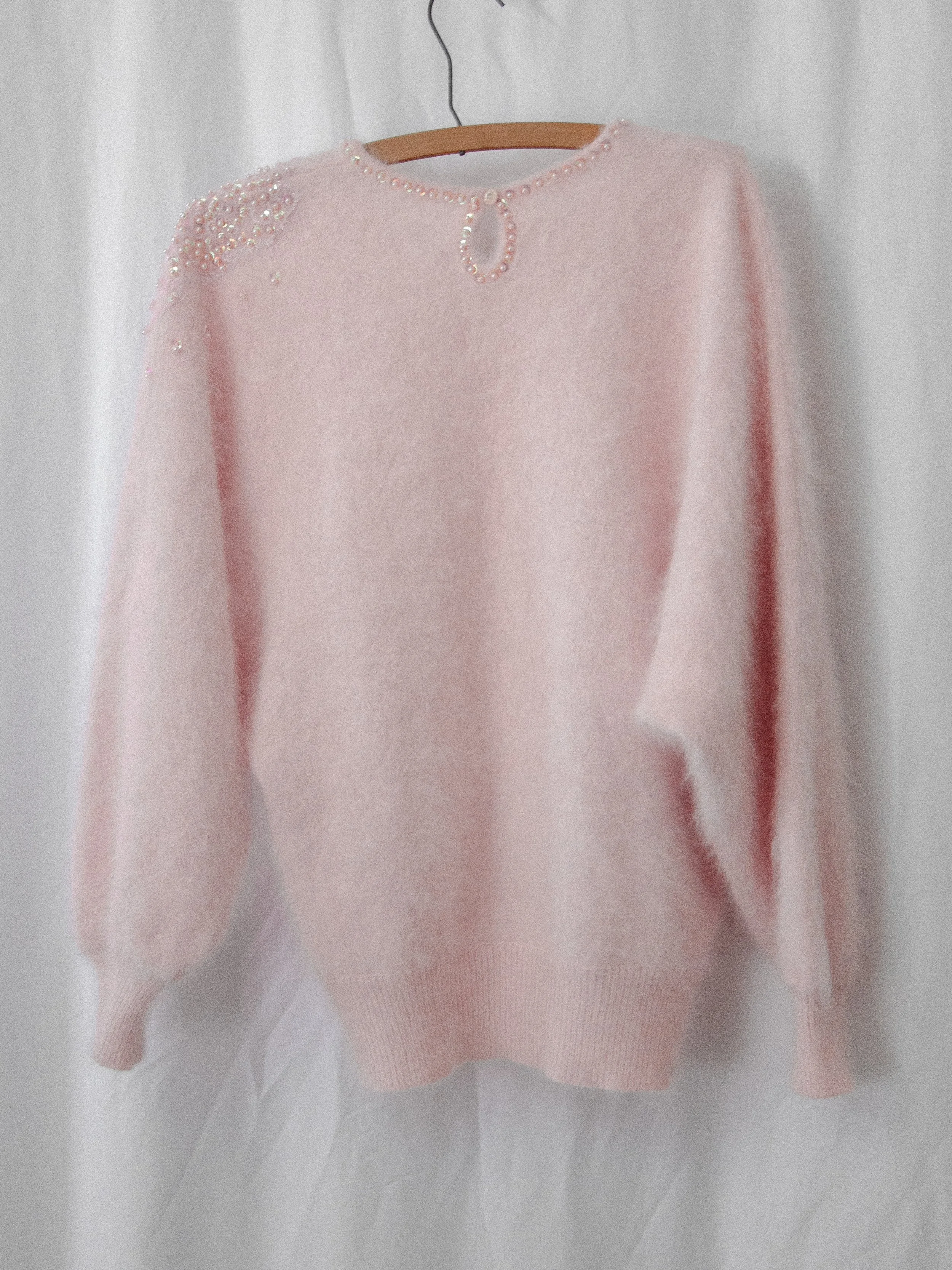 Back view of the 1980s pale pink angora sweater on a hanger, showing the beaded keyhole neckline.