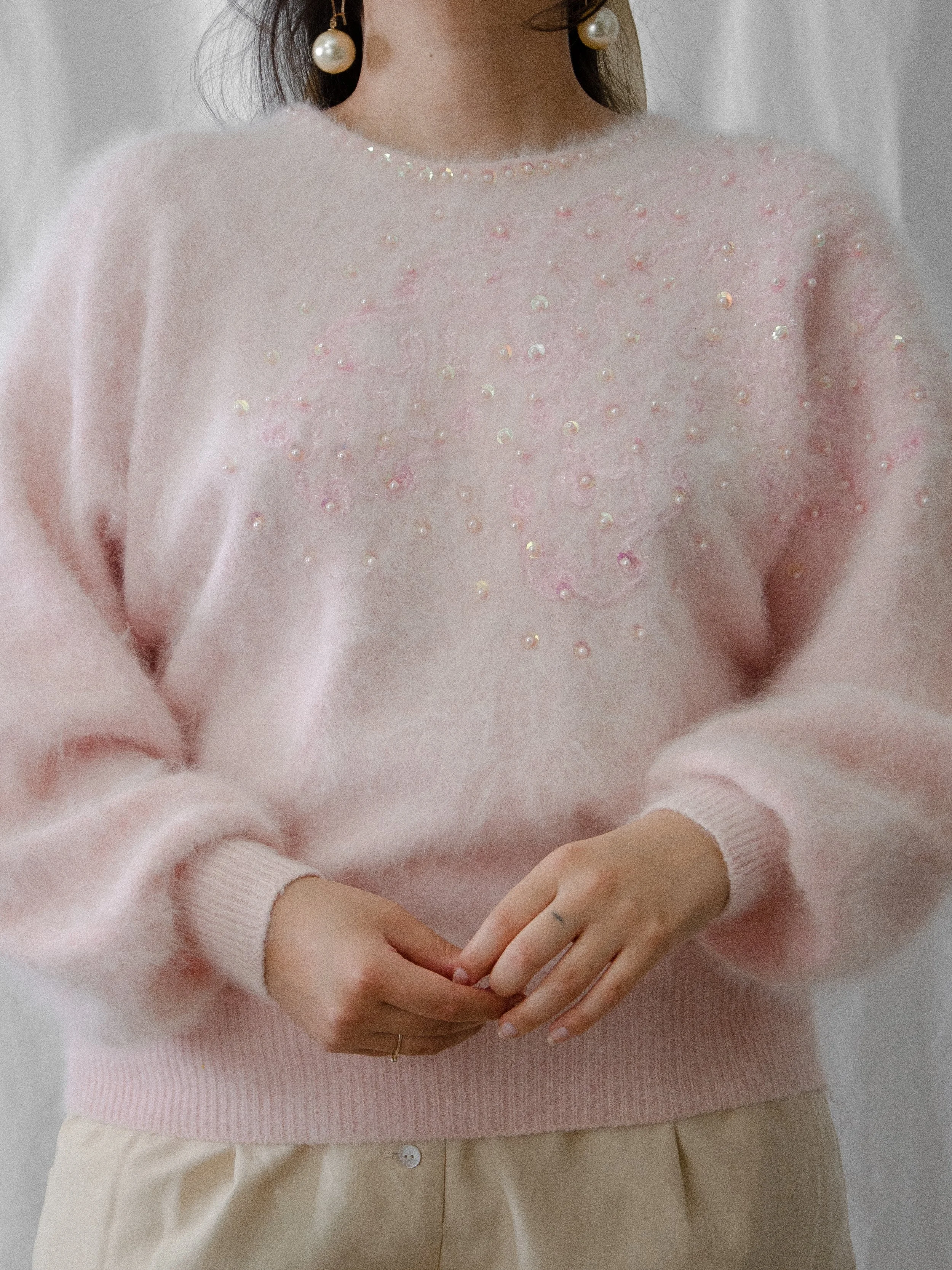 1980s pale pink angora dolman sleeve sweater on a model with hands clasped, showing the ribbed hem.
