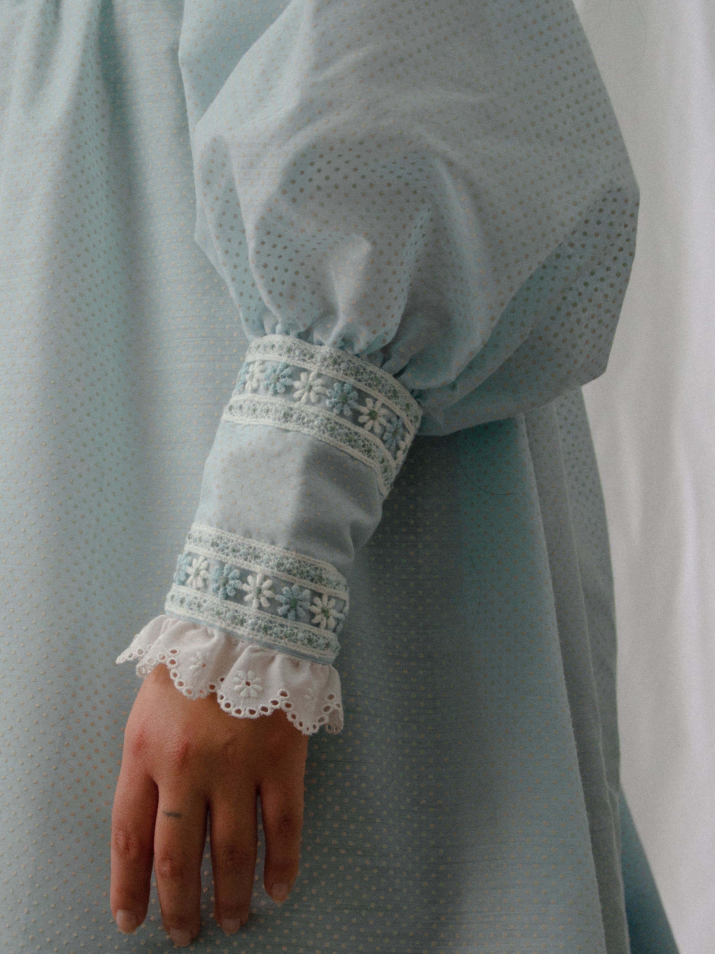 Close-up of the 1970s blue mini dress's puffed sleeve and daisy lace cuff with eyelet ruffle.
