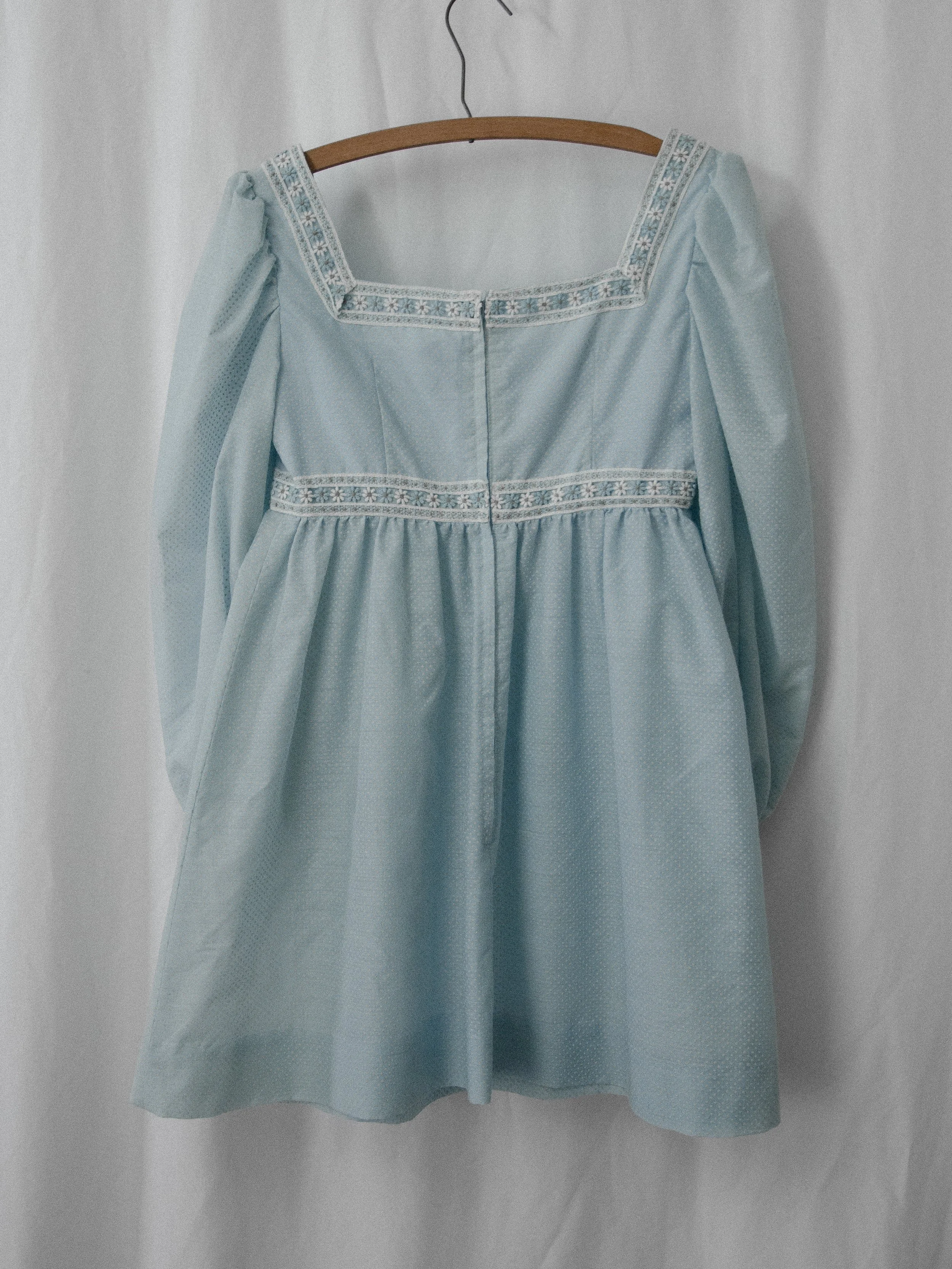 Back view of the 1970s sky blue mini dress on a hanger, showing the square lace back and zipper.