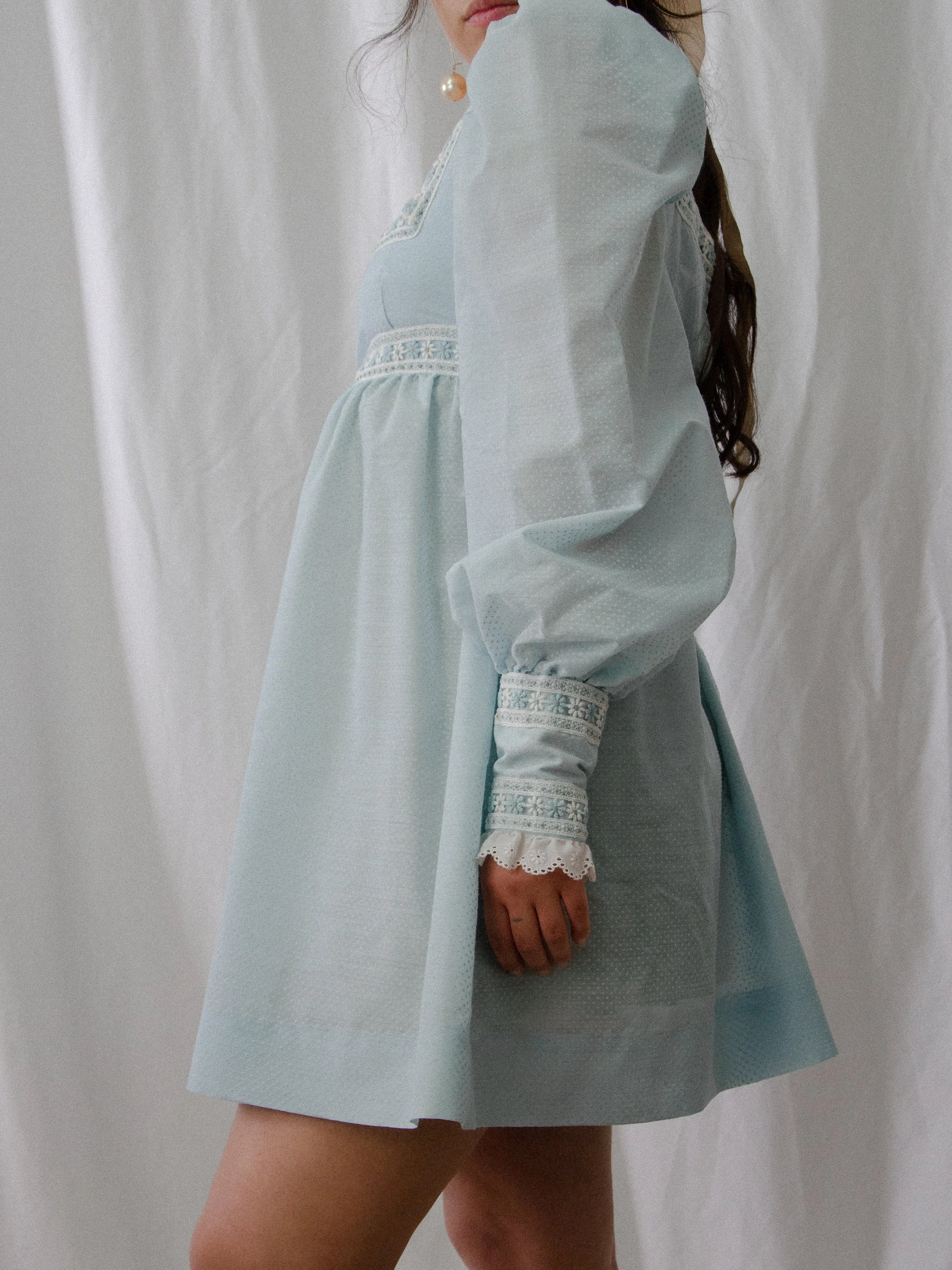 Side view of the 1970s sky blue Swiss dot mini dress on a model, showing the sleeve and short skirt.