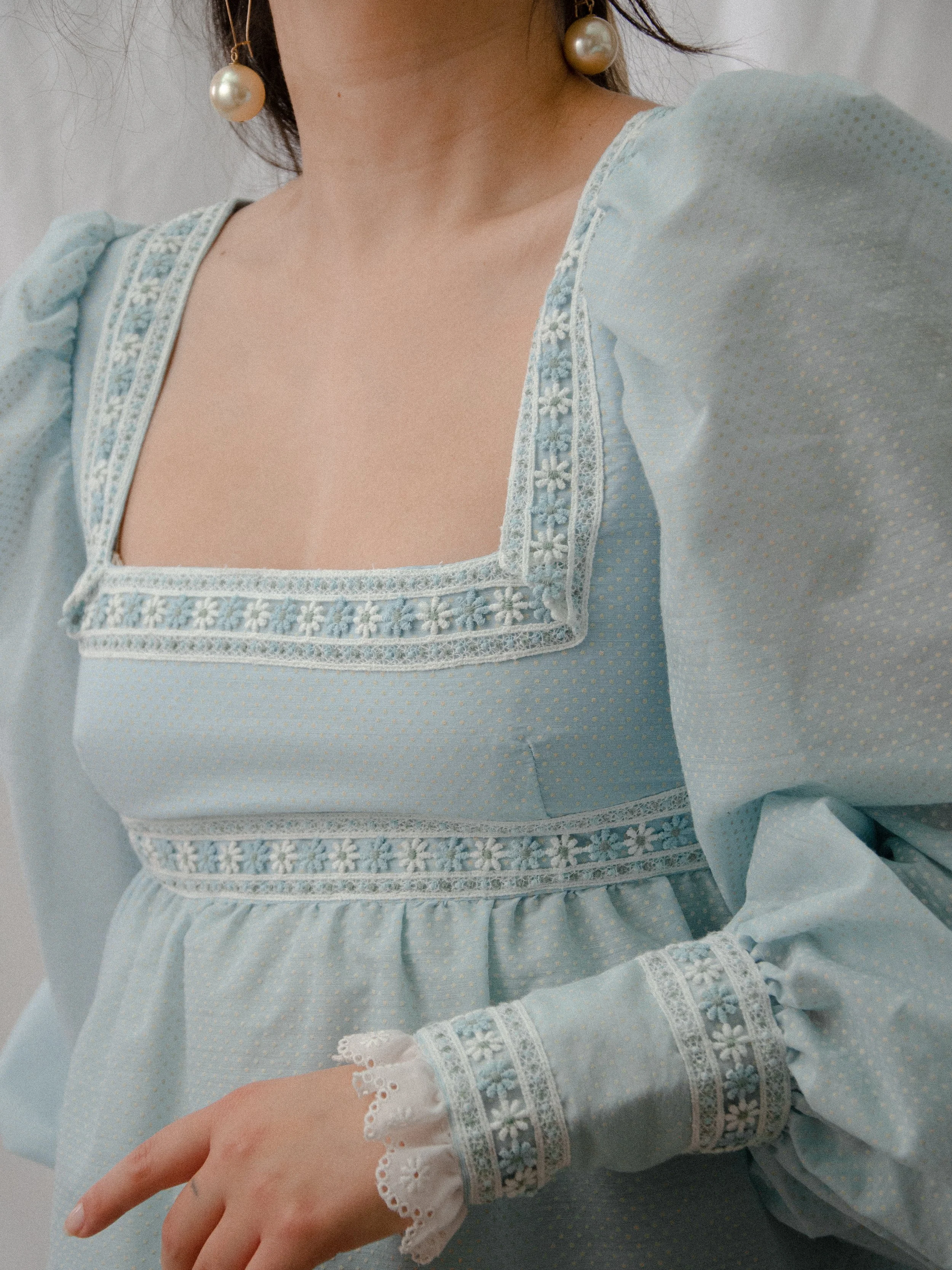 Close-up of the 1970s sky blue Swiss dot dress's square neckline trimmed with daisy floral lace.