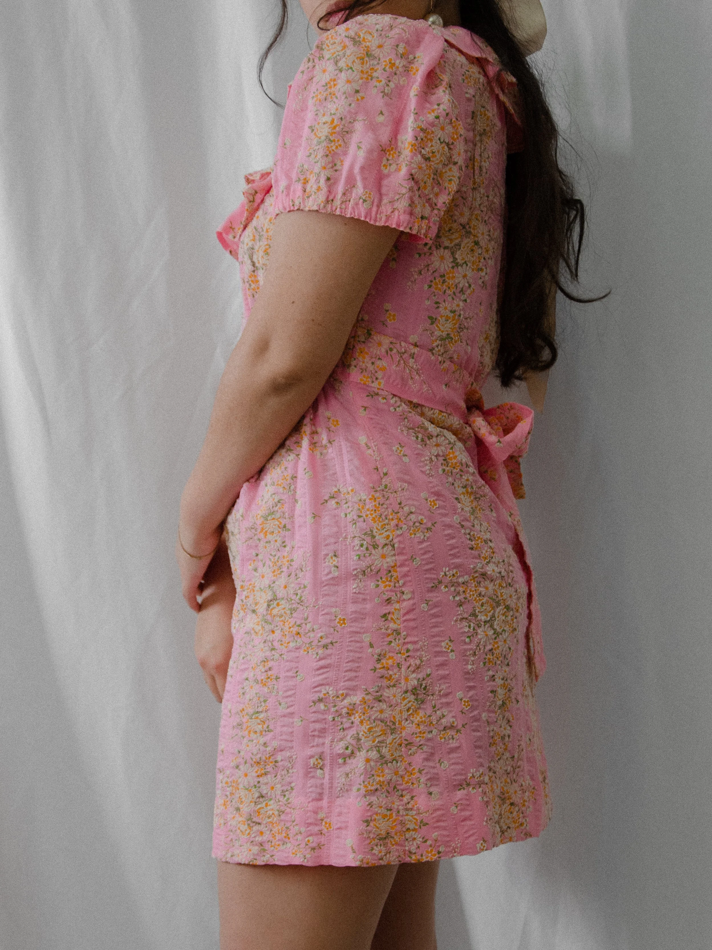 Side view of the 1970s pink floral mini dress on a model, showing the bow tied at the back waist.