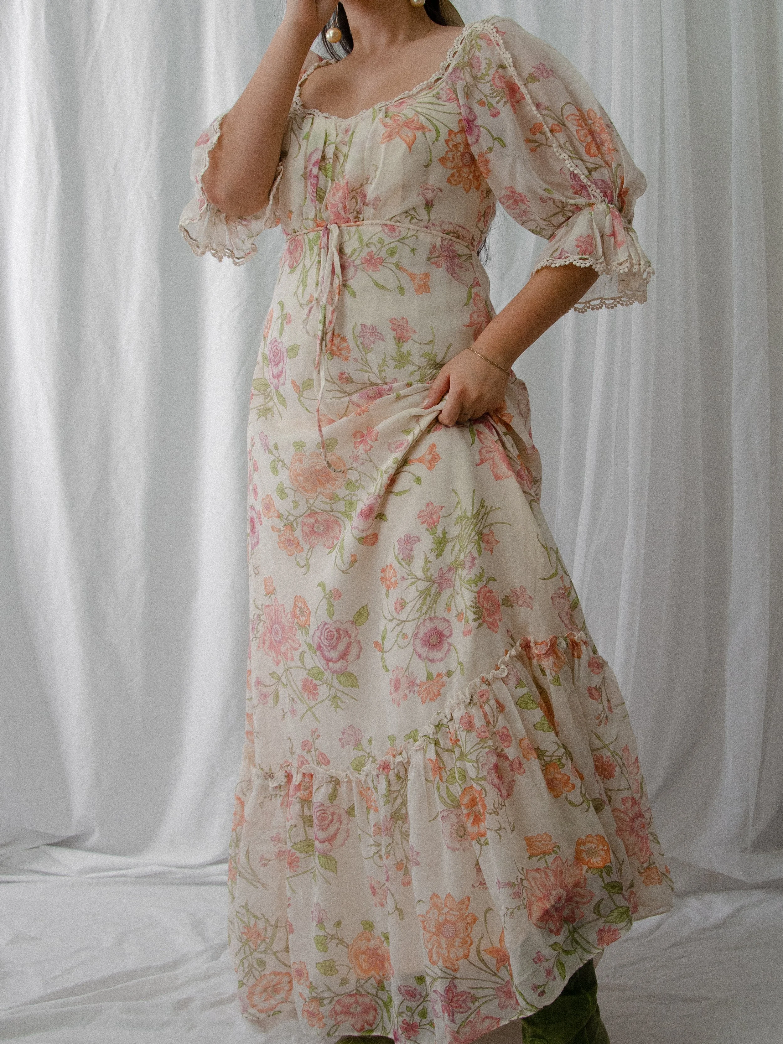 1970s floral voile maxi dress on a model with hand on hip, showing the puff sleeves and flounced hem.