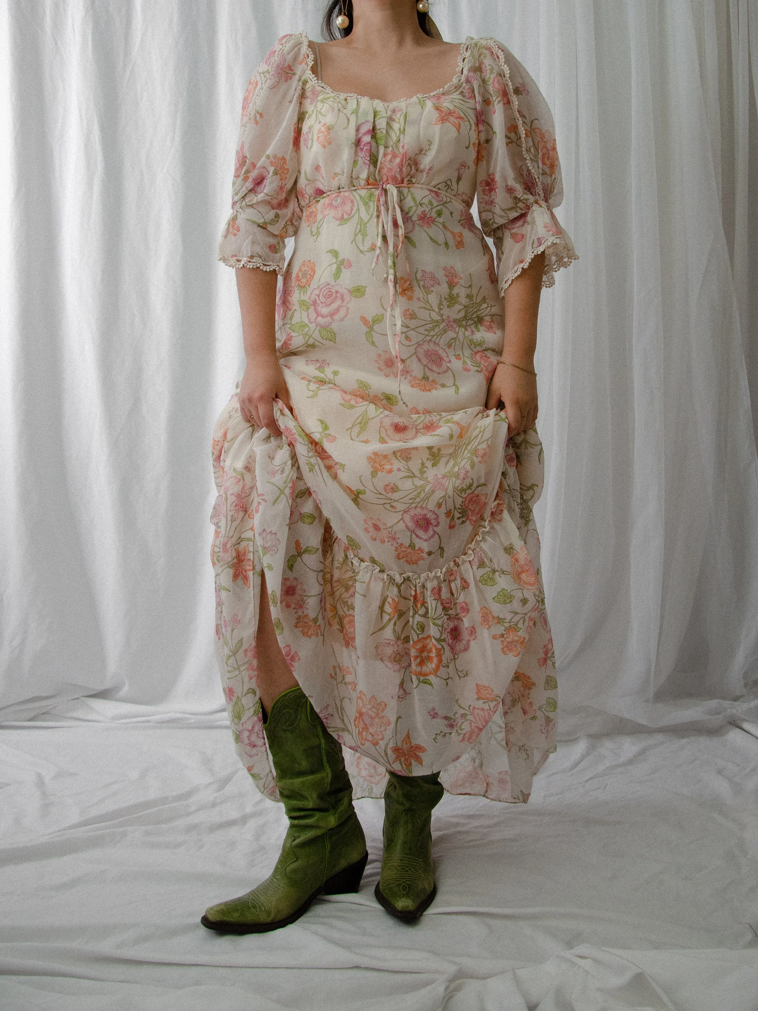 1970s cream floral maxi dress on a model lifting the skirt to reveal green cowboy boots.