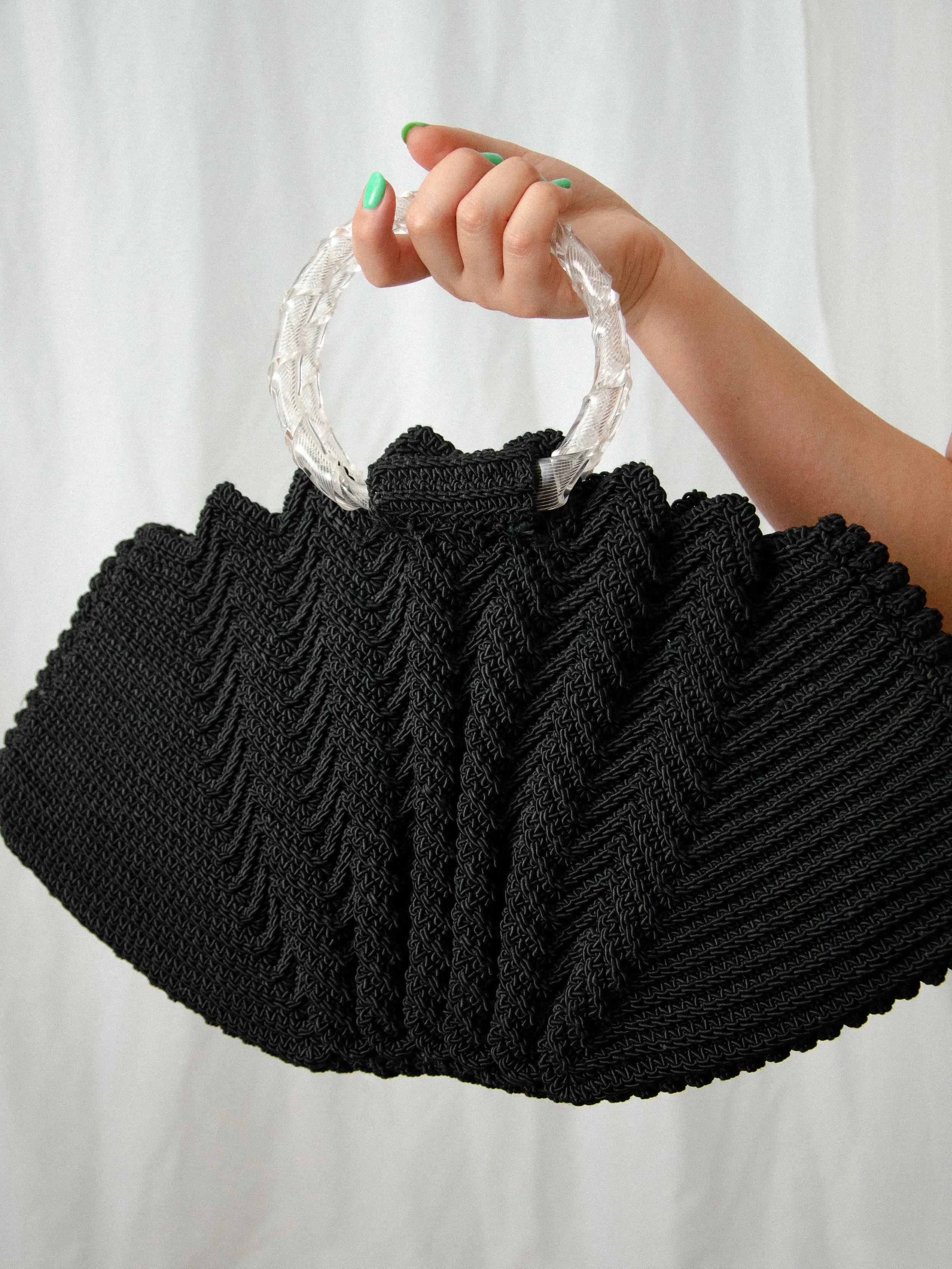 Close-up of the 1940s black crochet clamshell bag held by its twisted lucite hoop handle.