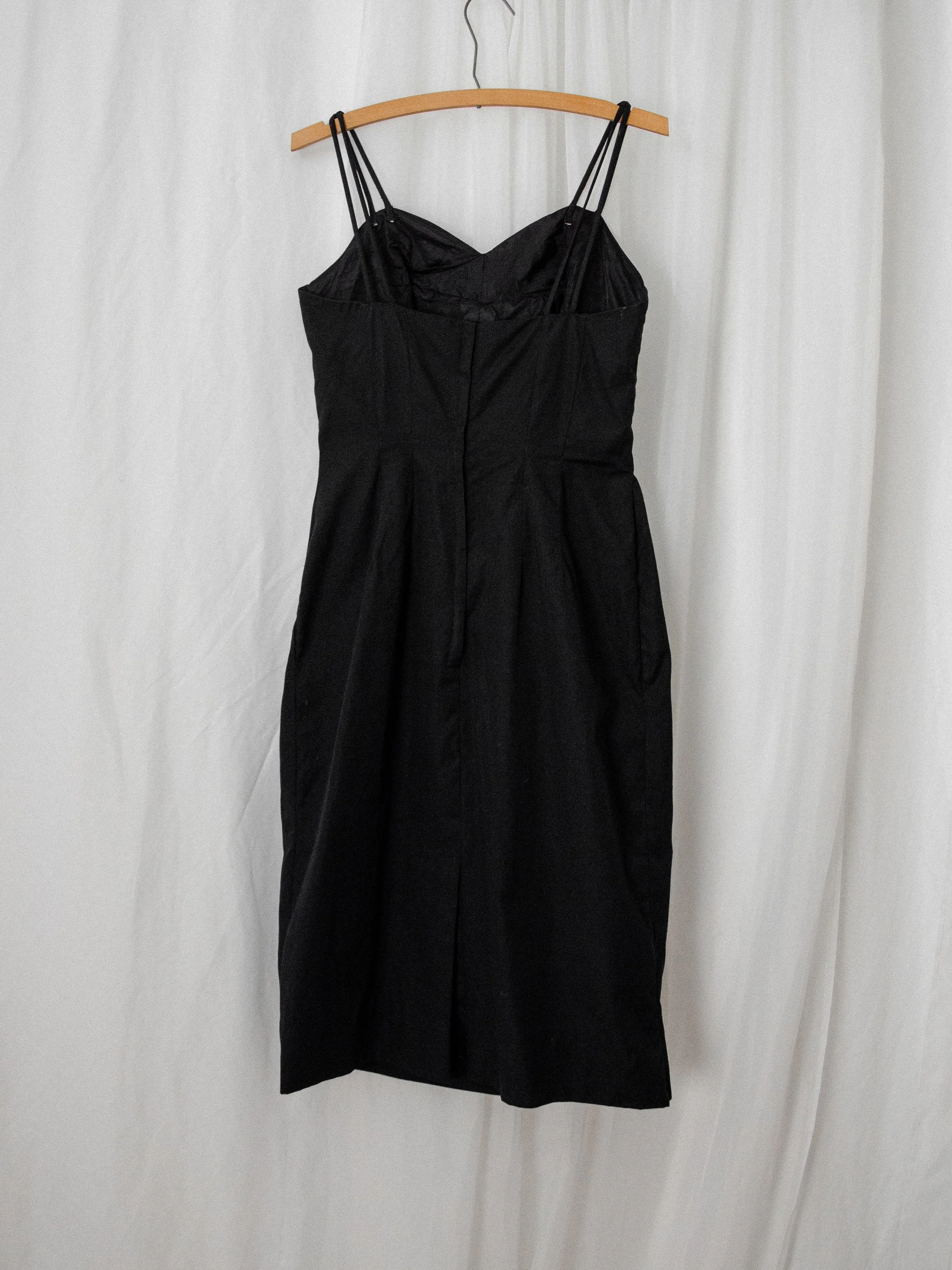 Back view of the 1950s black cotton wiggle dress on a hanger, showing the metal zipper and double straps.