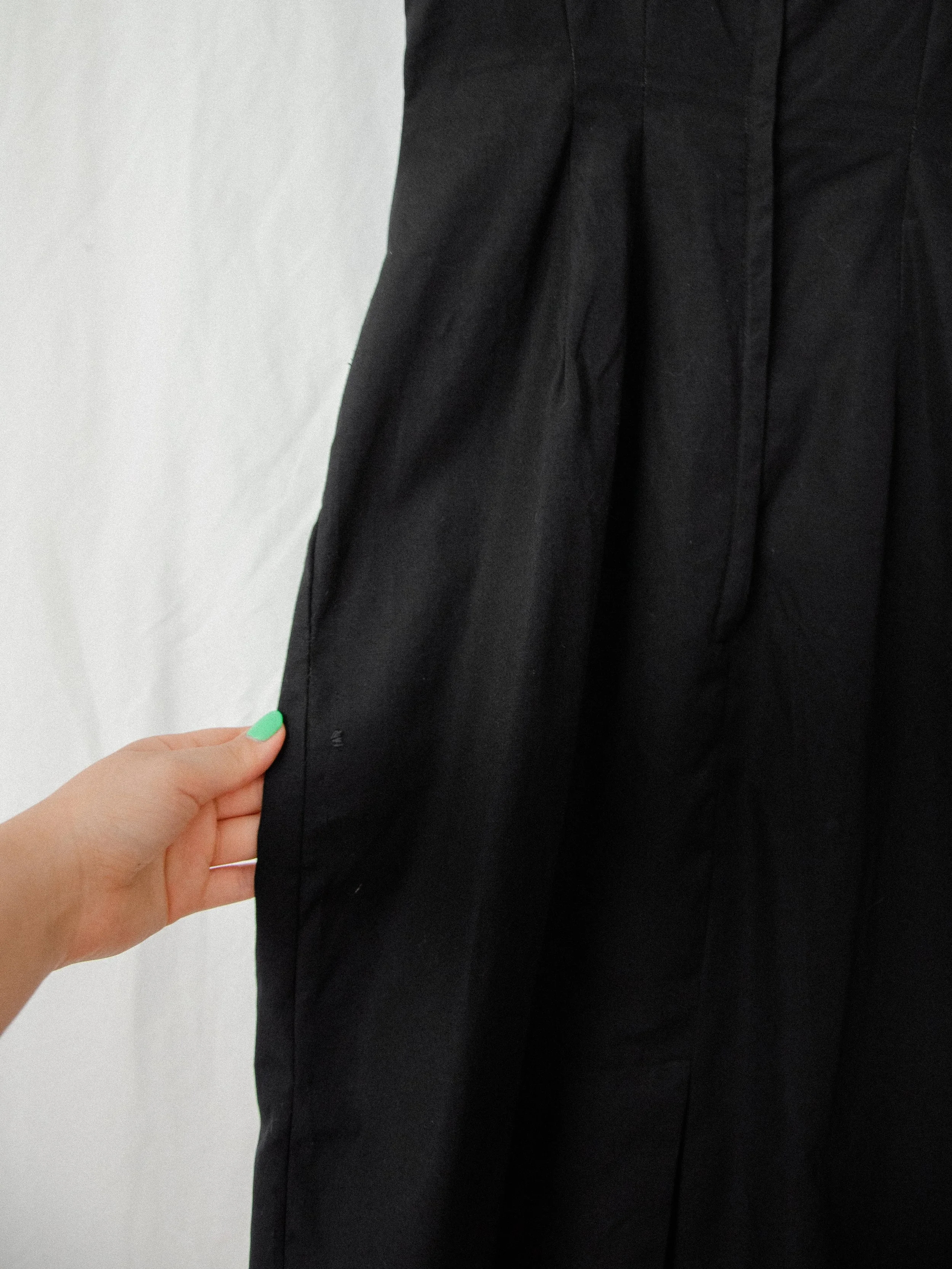 Detail of the 1950s black wiggle dress back skirt held at the side, showing a small mend near the edge.