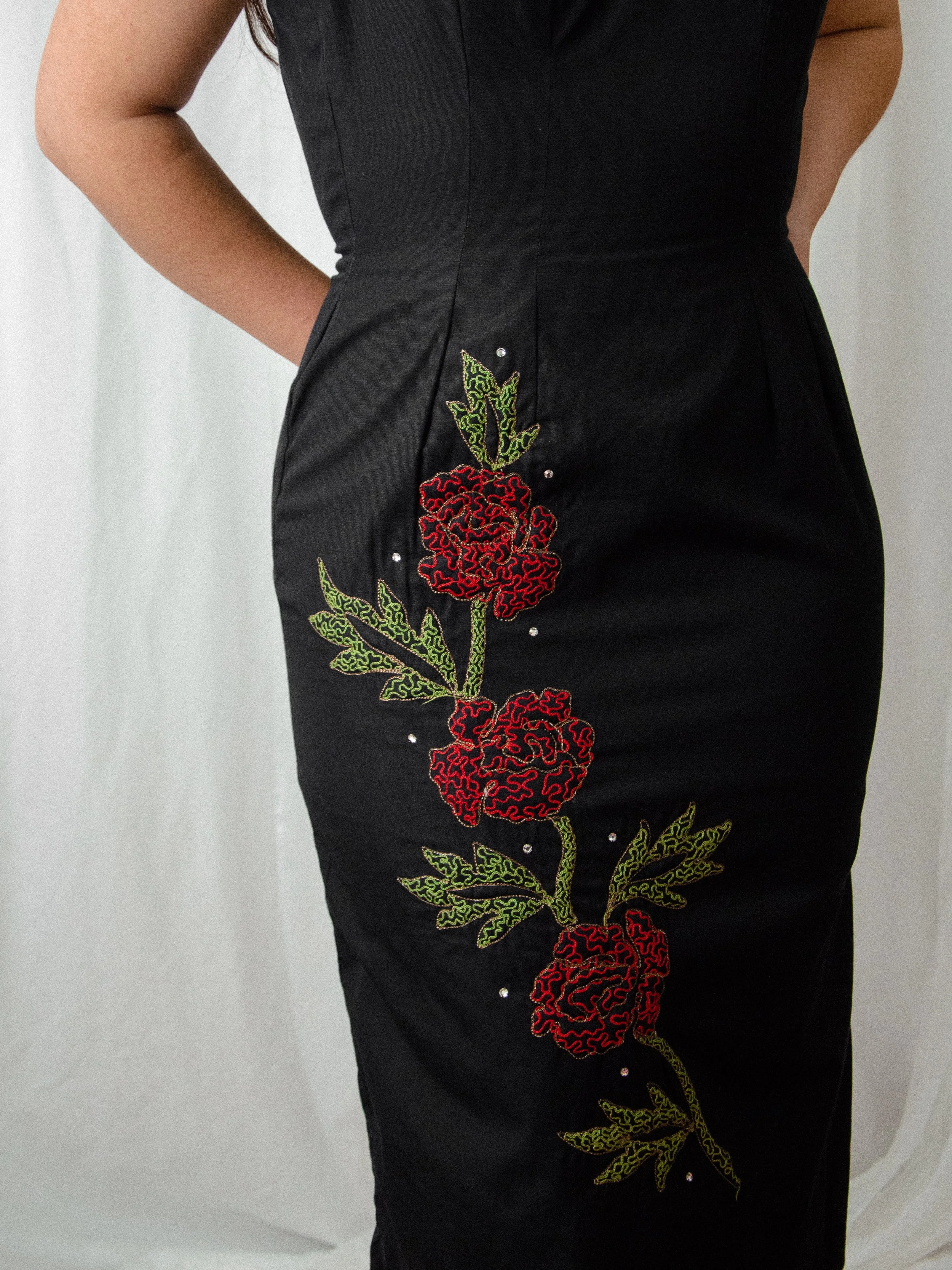 Close-up of the 1950s black wiggle dress skirt, showing red embroidered roses with gold outline and rhinestones.