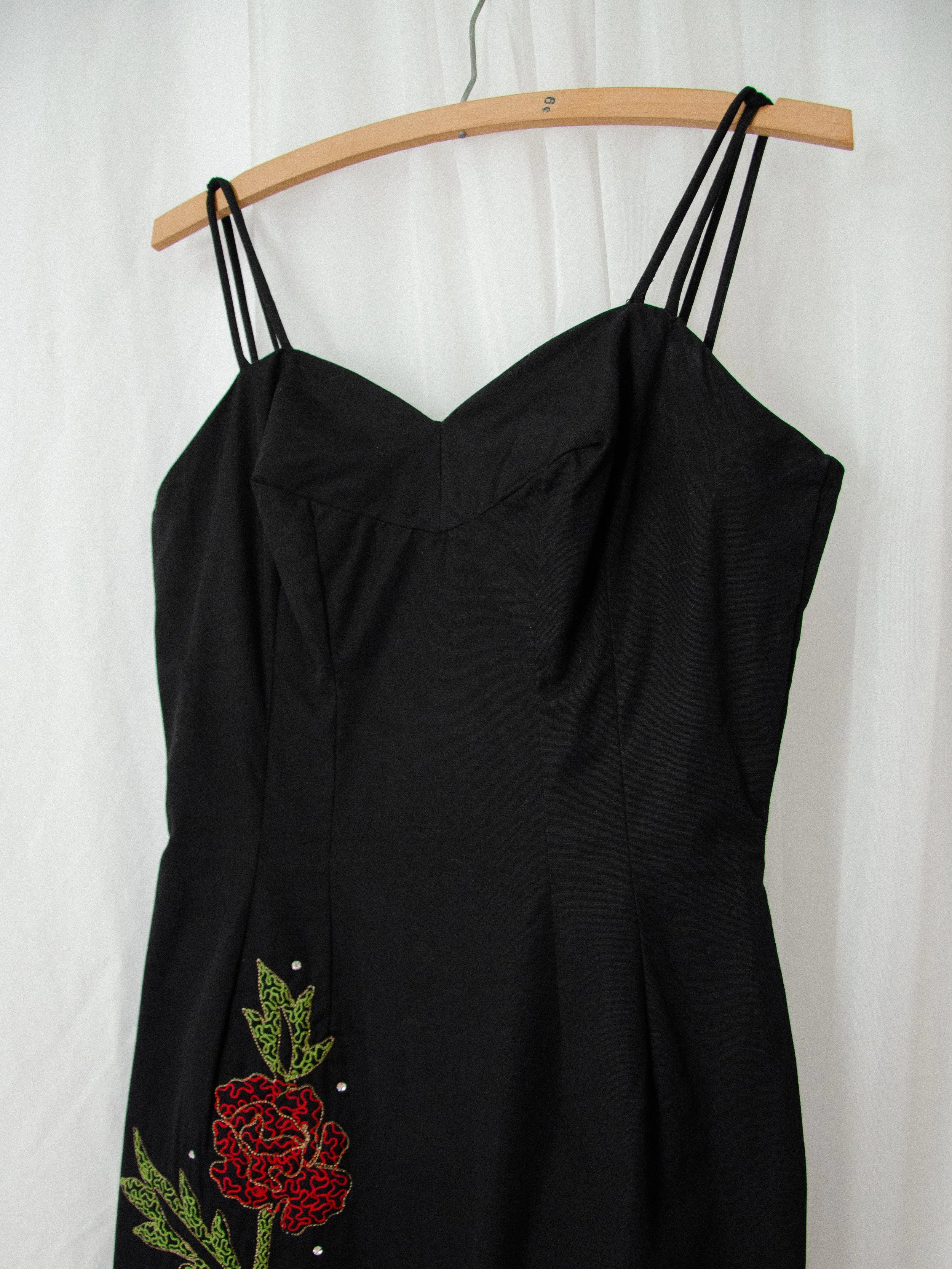Close-up of the 1950s black wiggle dress bodice on a hanger, showing the sweetheart neckline and rose embroidery.
