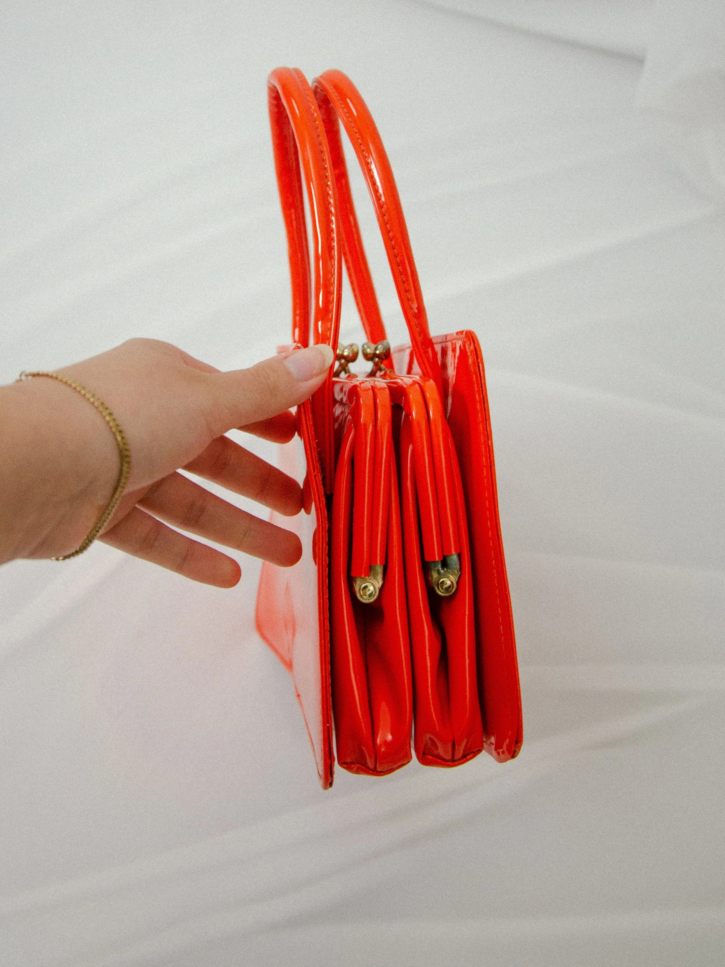 Side view of the 1960s orange handbag held by hand, showing the two compartments with gold clasps.