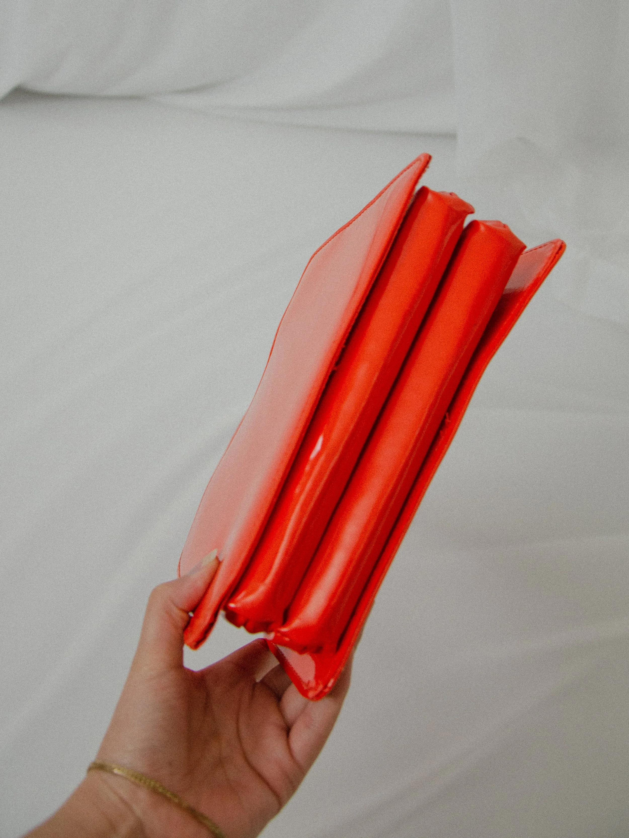 Bottom view of the 1960s orange vinyl handbag held by hand, showing the expandable compartments.
