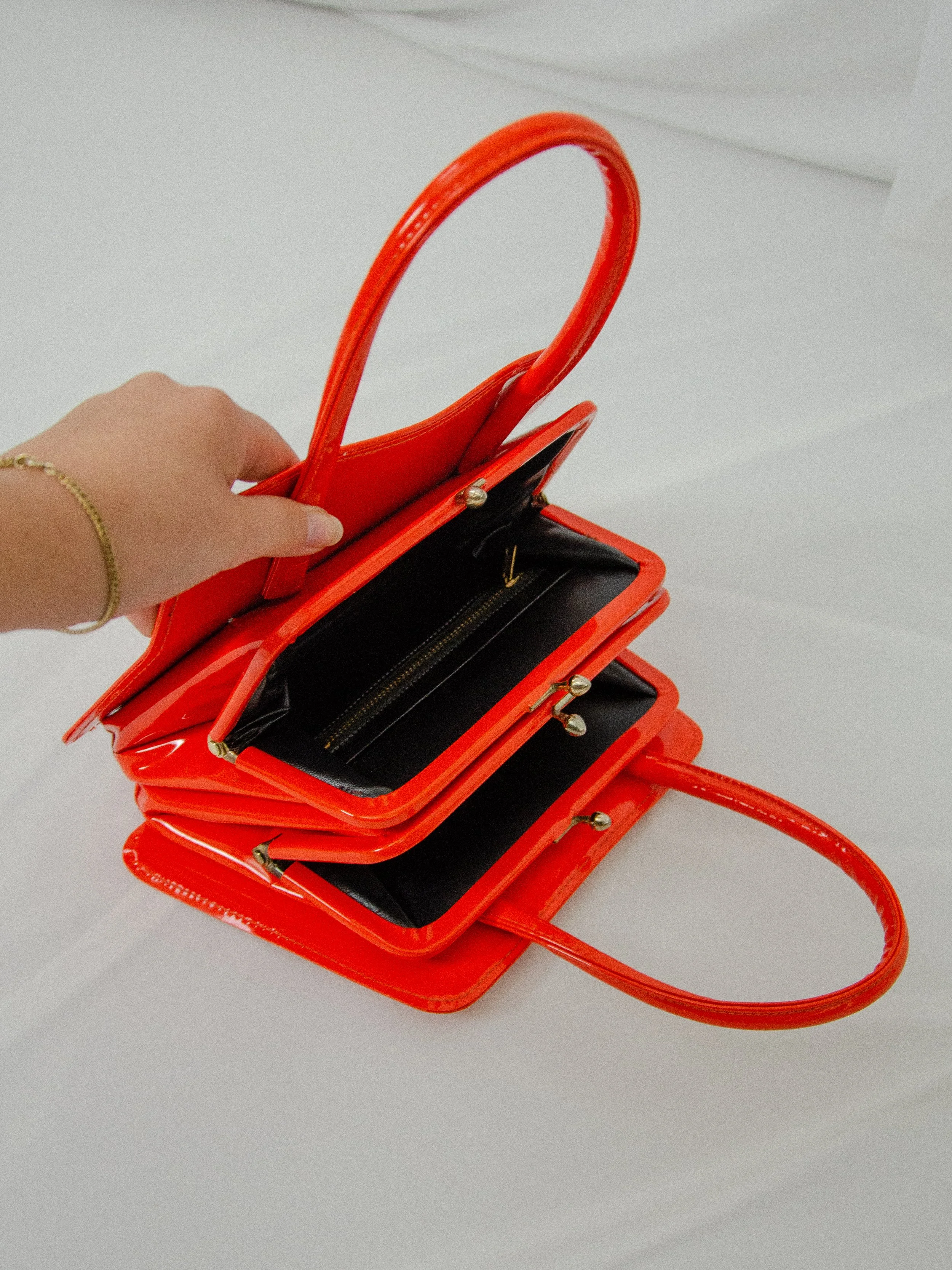 1960s orange vinyl handbag opened by hand, showing the black lining inside both compartments.