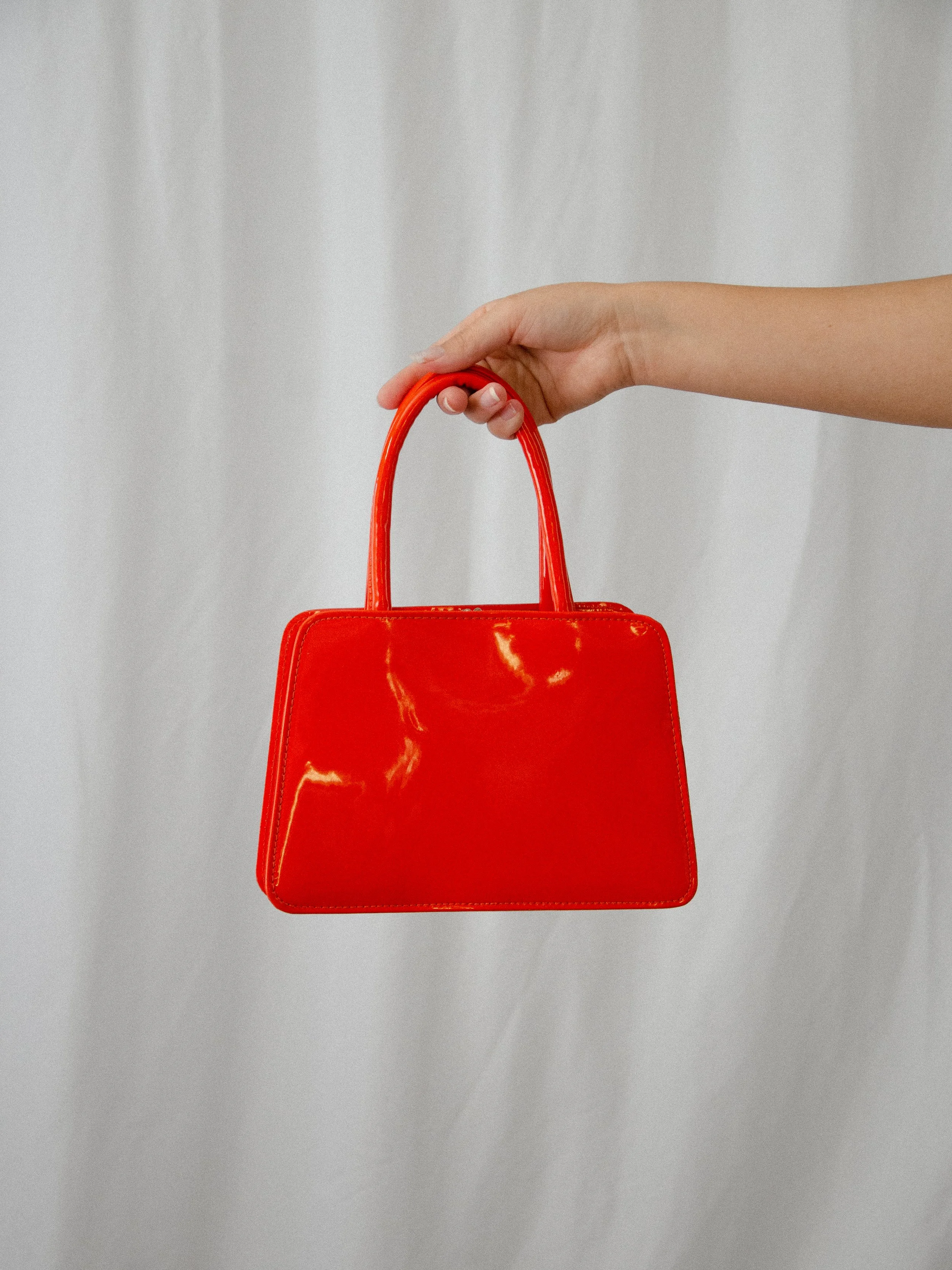 Back view of the 1960s glossy orange vinyl handbag held up by its top handle.