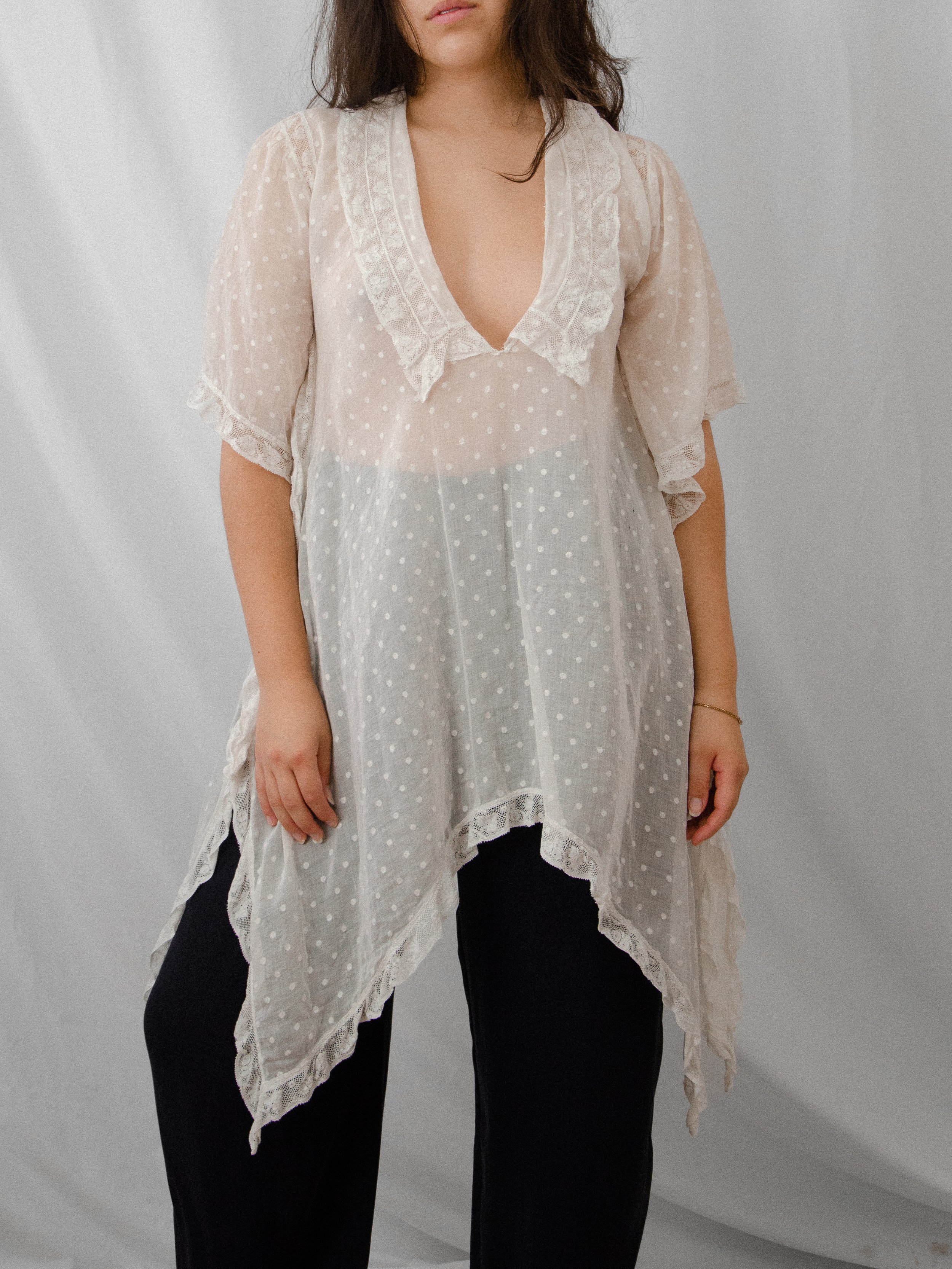 Front view of the 1920s white Swiss dot angel sleeve top on a model over black trousers.