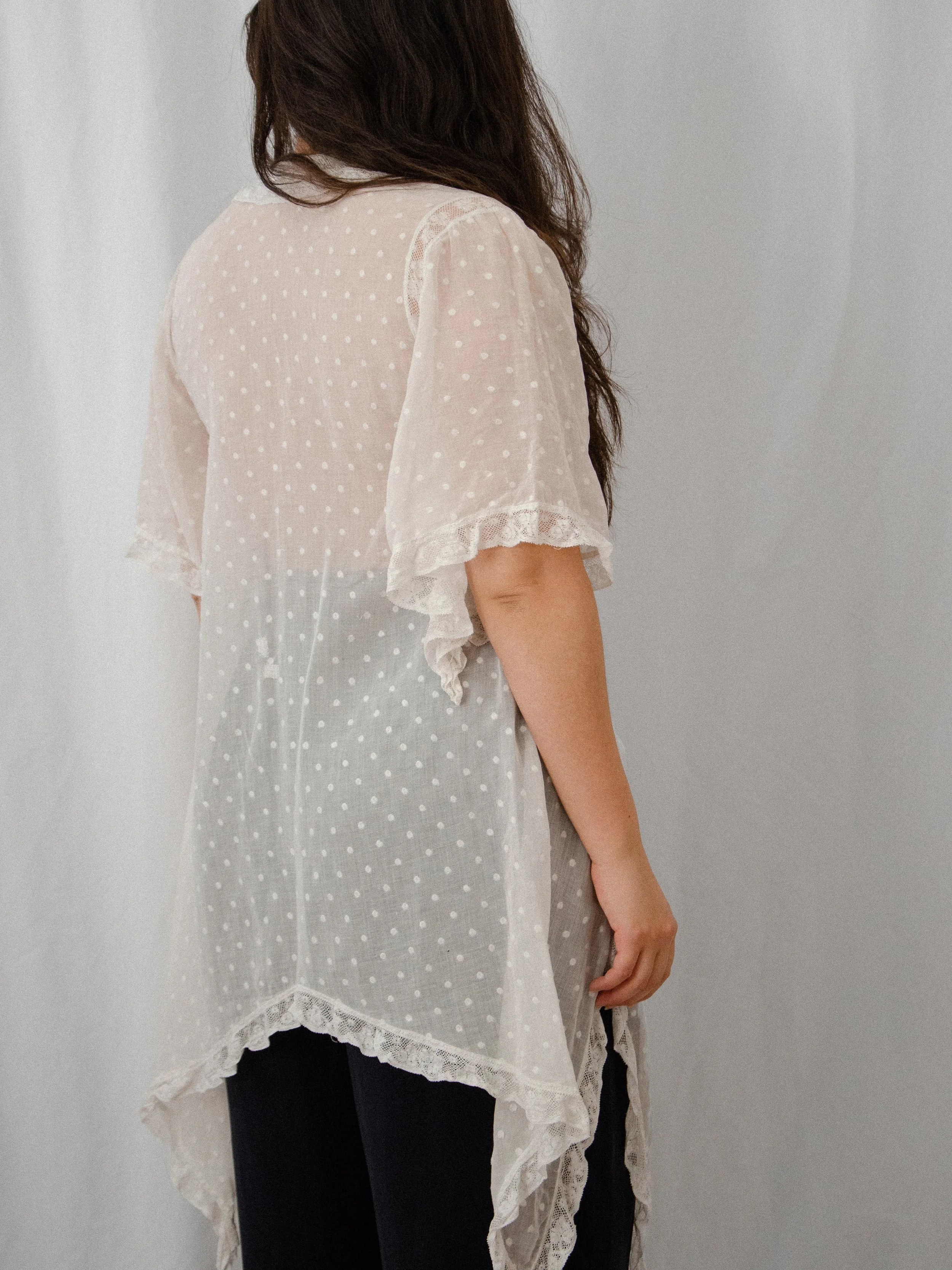 Back view of the 1920s sheer white Swiss dot top on a model, showing the lace-trimmed sleeves and hem.