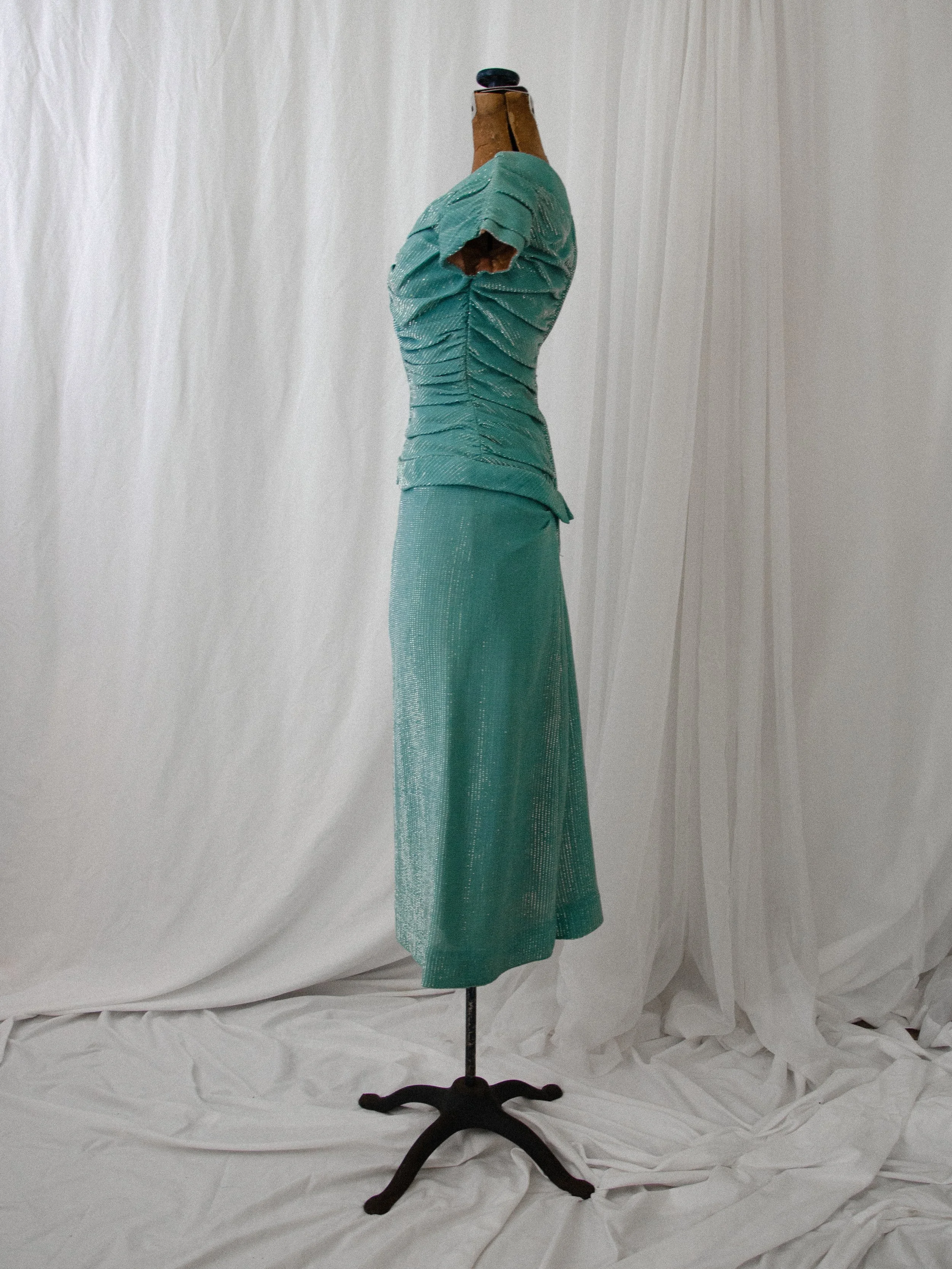 Side view of the late 1940s turquoise lamé dress on a dress form, showing the longline peplum silhouette.