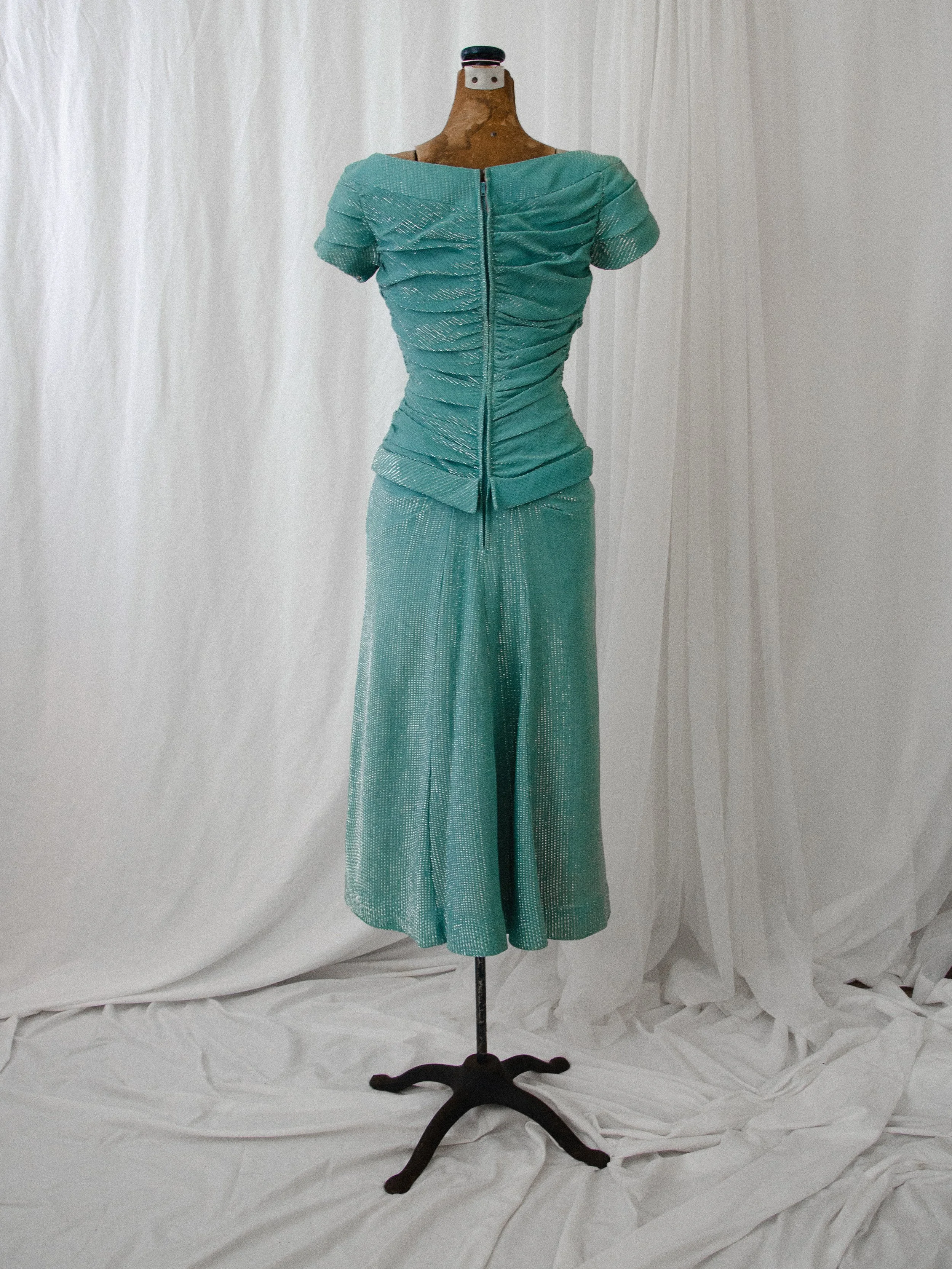 Back view of the late 1940s turquoise lamé dress on a dress form, showing the back zipper and peplum.