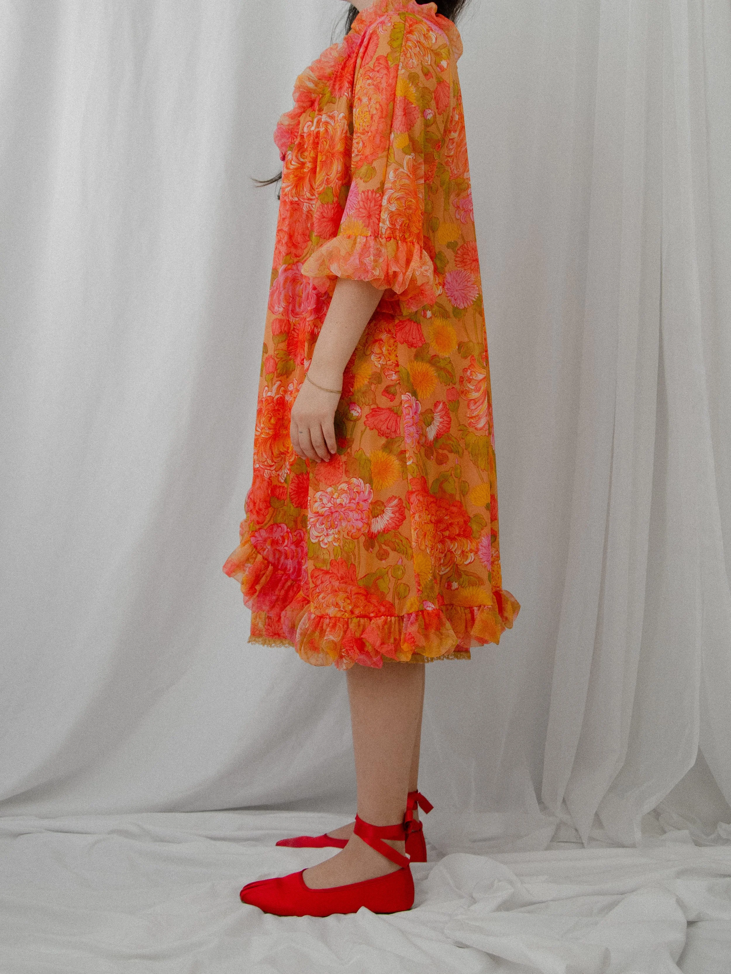 Side view of the 1960s orange floral nylon peignoir robe on a model, showing the ruffled hem.