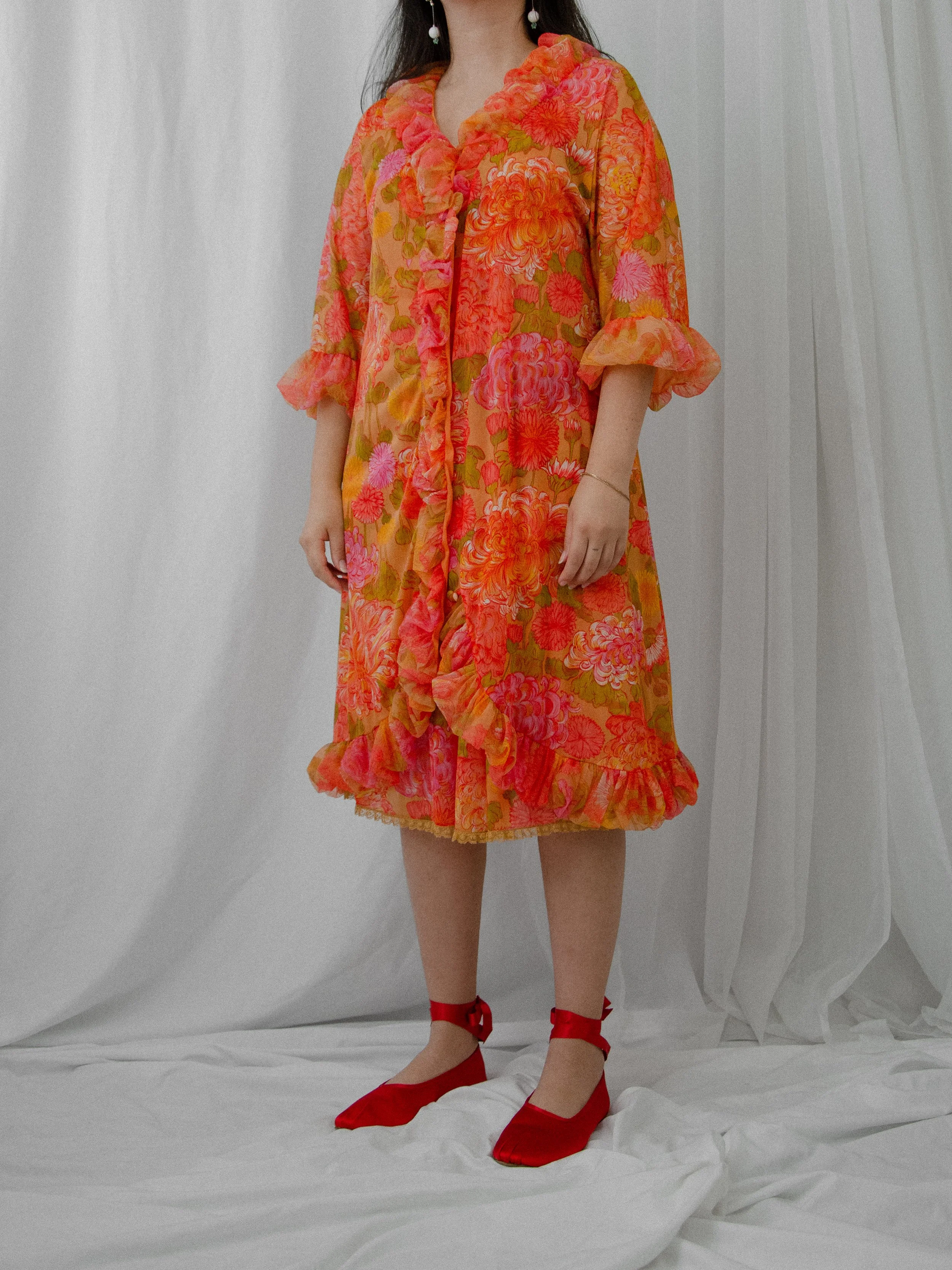 1960s orange chrysanthemum print peignoir robe worn closed on a model, showing puffy ruffled cuffs.