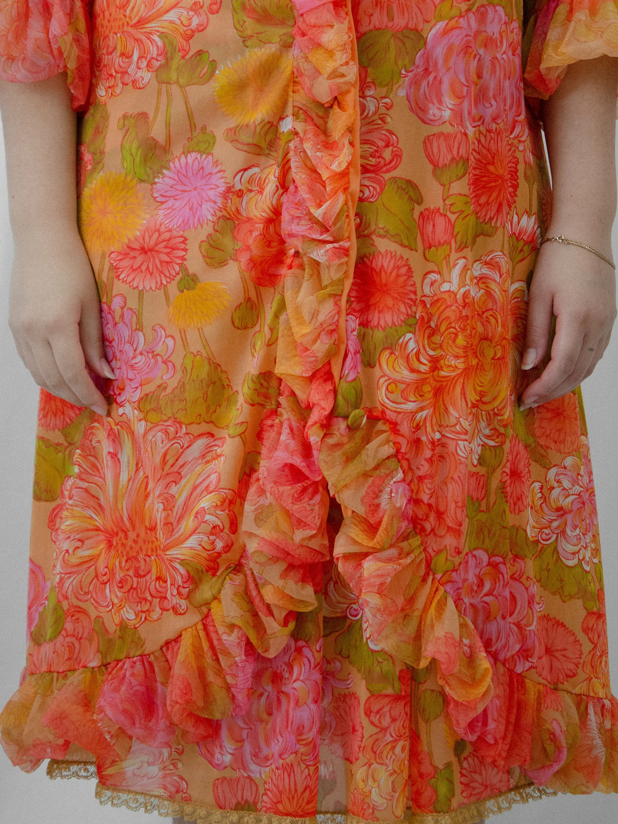 Detail of the 1960s orange floral nylon peignoir robe's ruffled front edge and lace-trimmed hem.