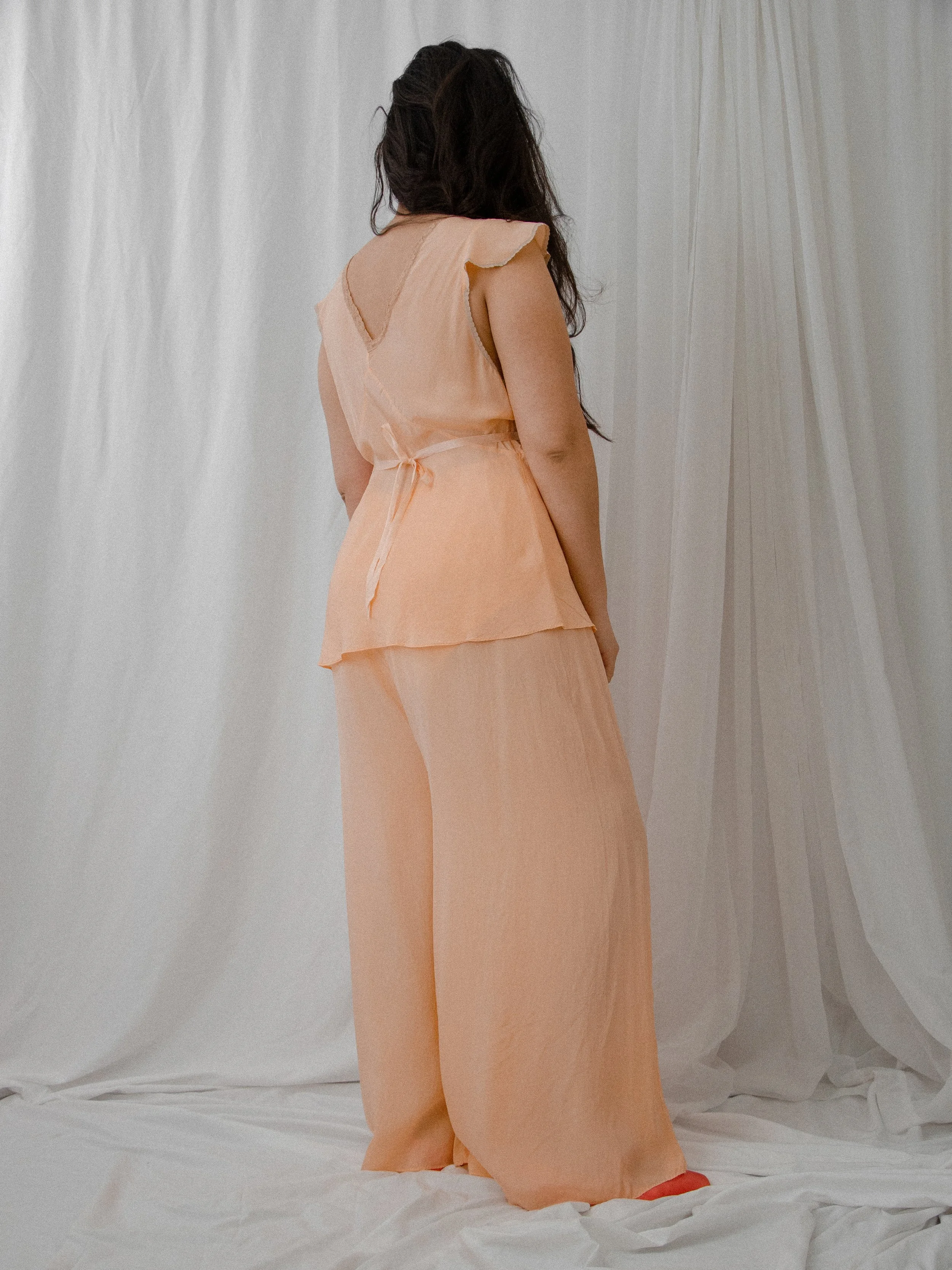 Back view of the 1930s peach silk pajama set on a model, showing the V-back and silk waist tie.