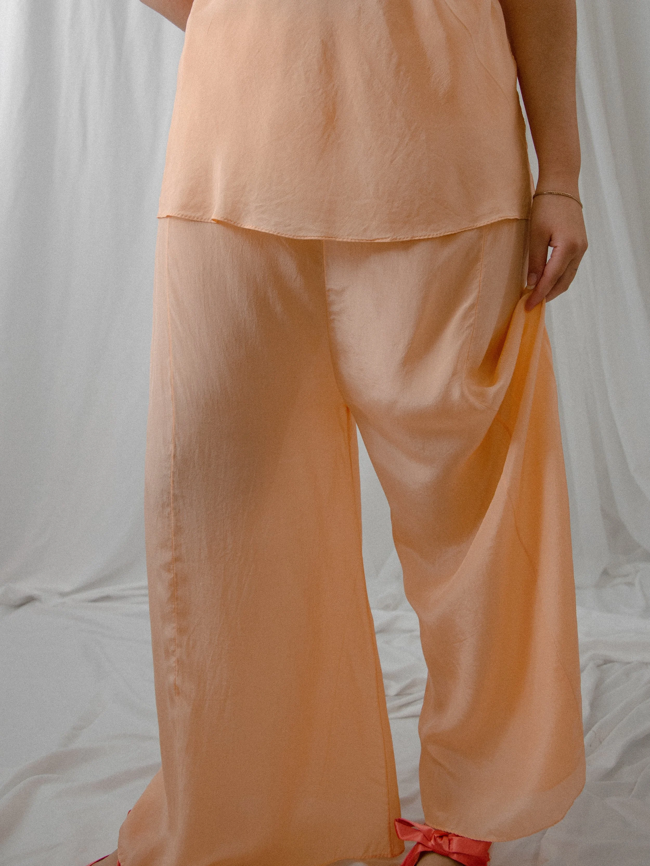 Detail of the 1930s peach silk high-rise pajama pants on a model, showing the wide drapey legs.