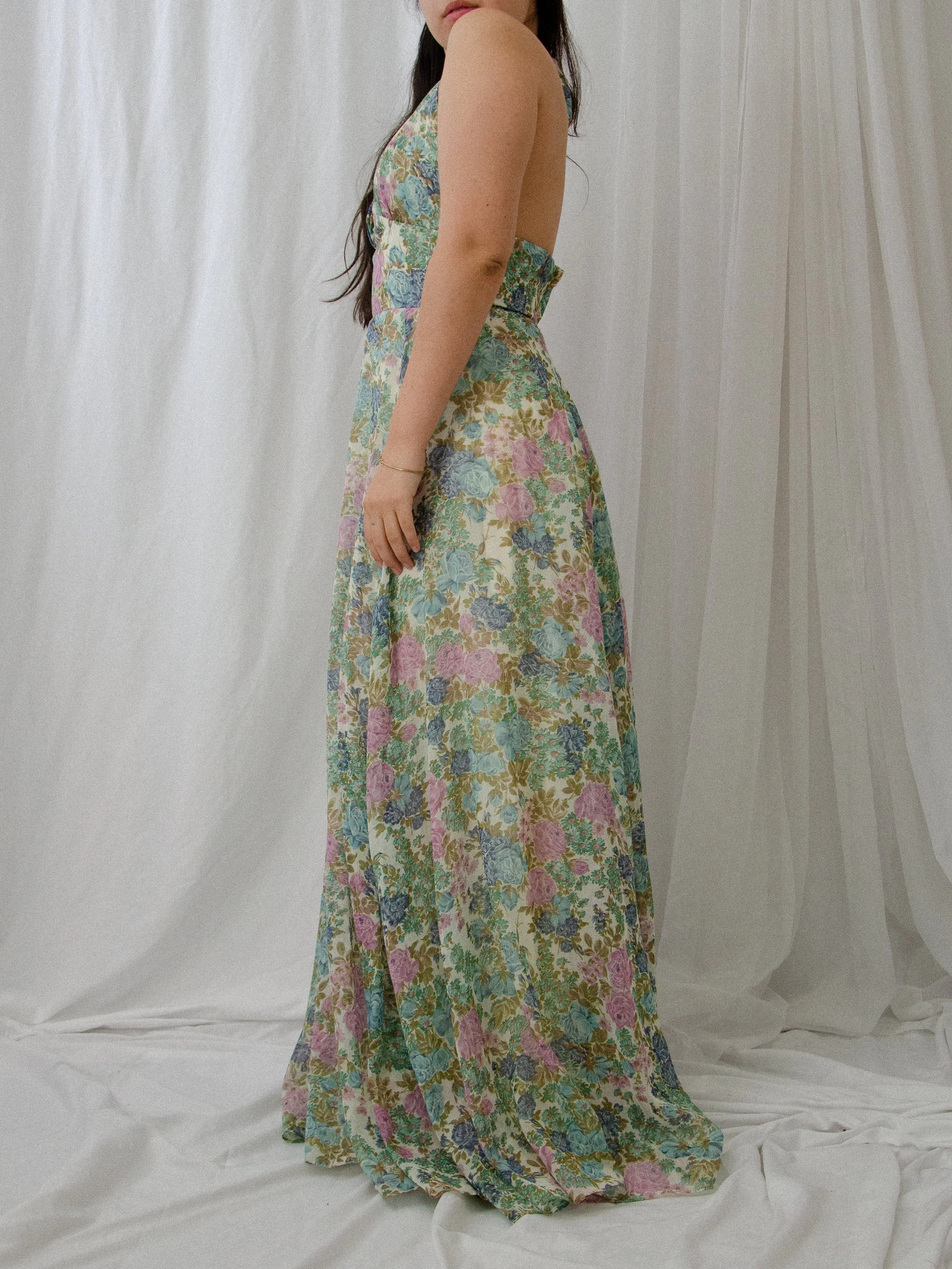 Side view of the 1970s floral halter maxi dress on a model, showing the open back and long skirt.