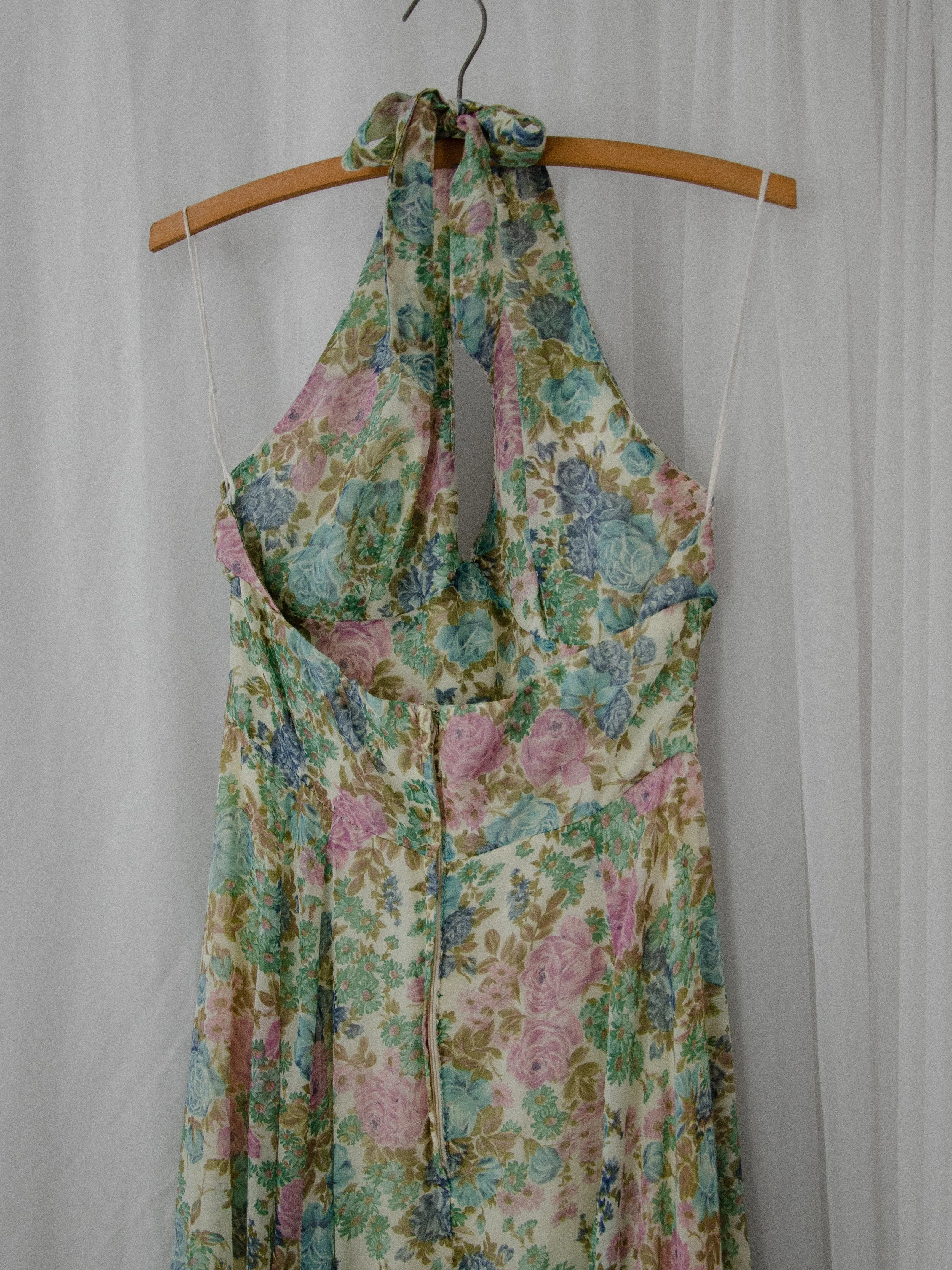 Back view of the 1970s floral halter dress on a hanger, showing the halter tie, keyhole and long zipper.