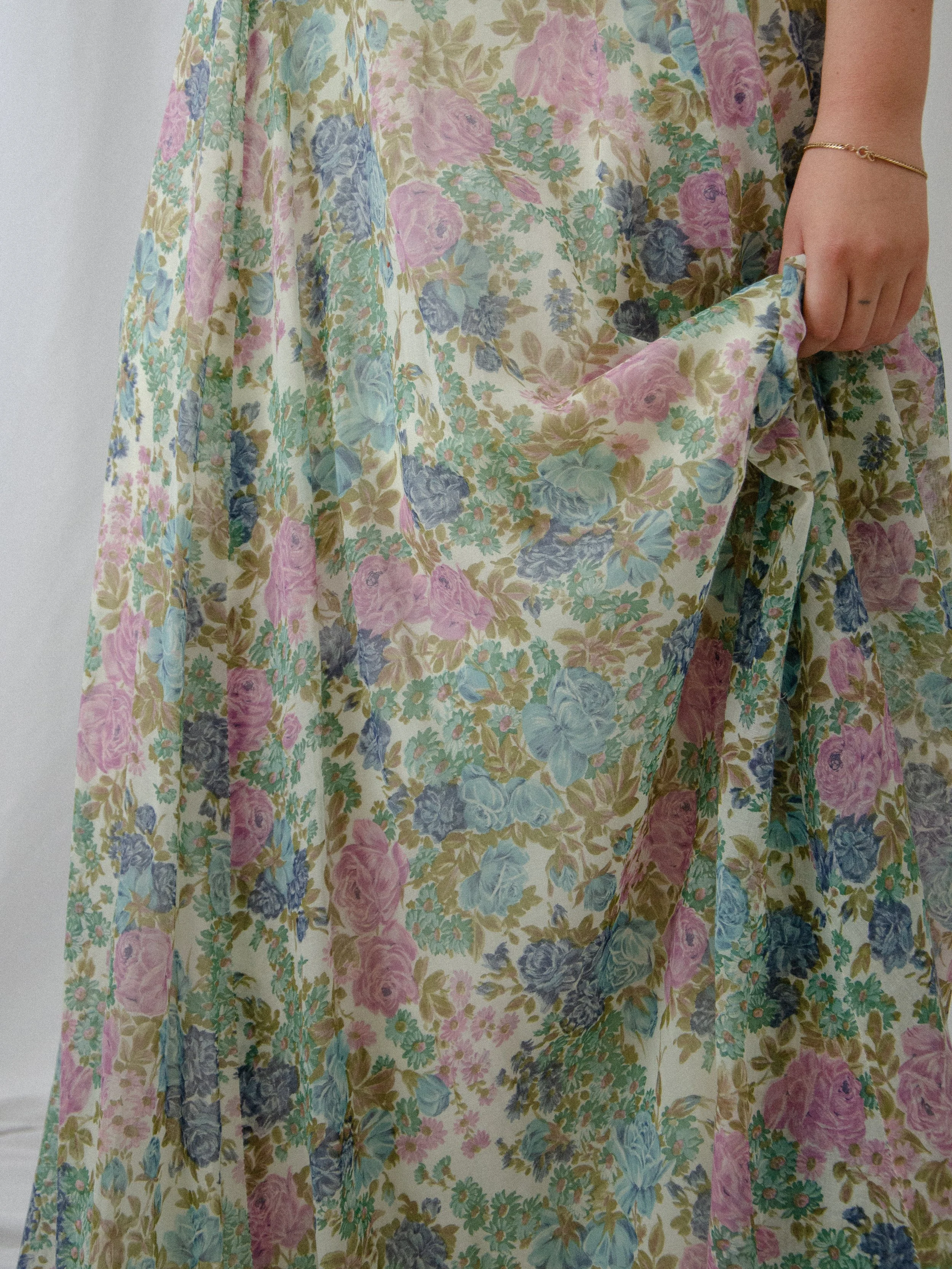 Detail of the 1970s floral voile maxi skirt lifted by hand, showing the rose print and lining.