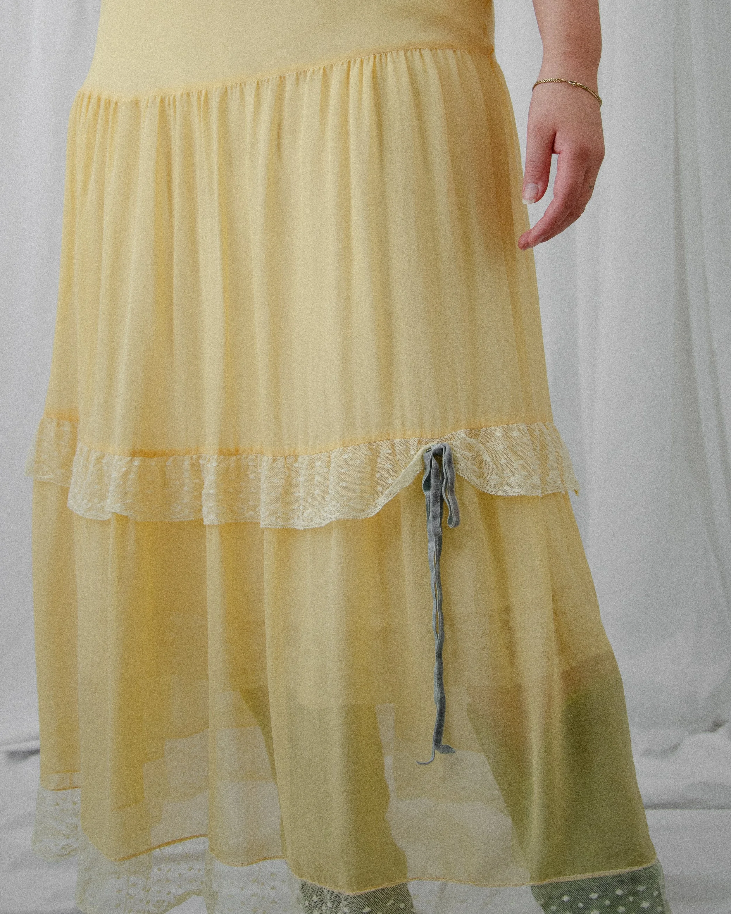 Detail of the 1940s canary yellow silk dress's tiered skirt with lace trims and a blue velvet bow.